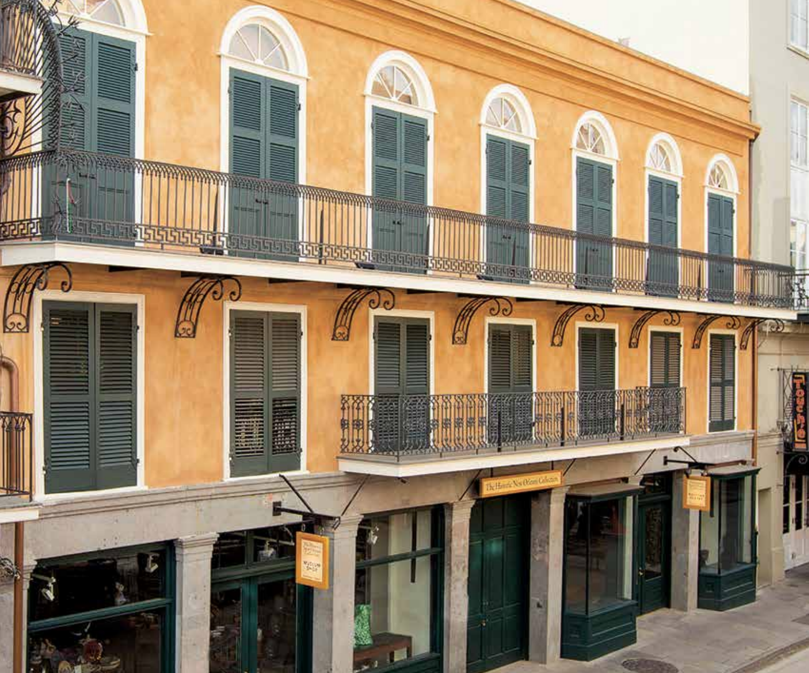 A multi-story building with orange and yellow walls, green shutters on windows, and black wrought iron balconies.