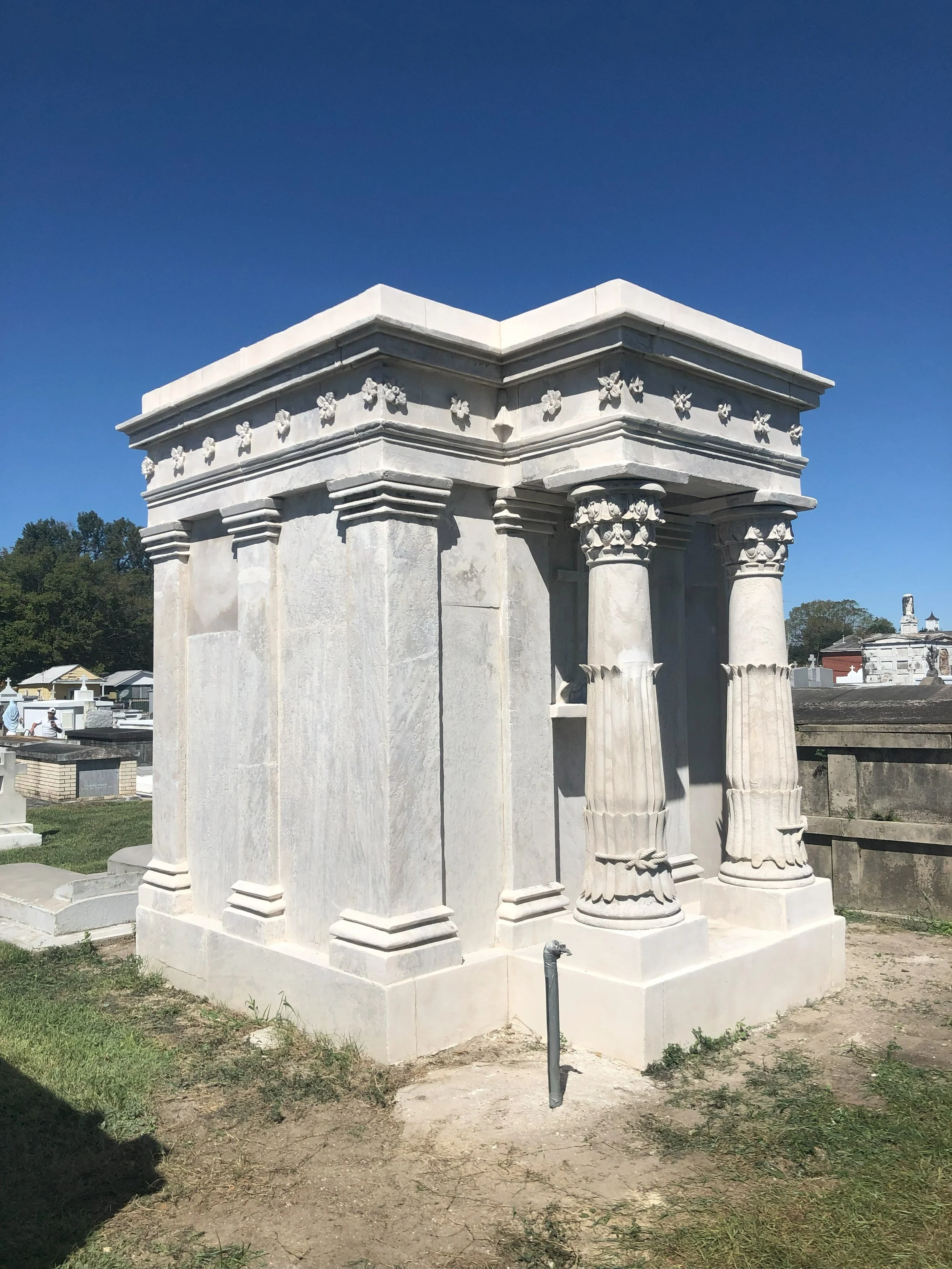 A white marble mausoleum with classical columns and decorative details, located in a cemetery under a clear blue sky.