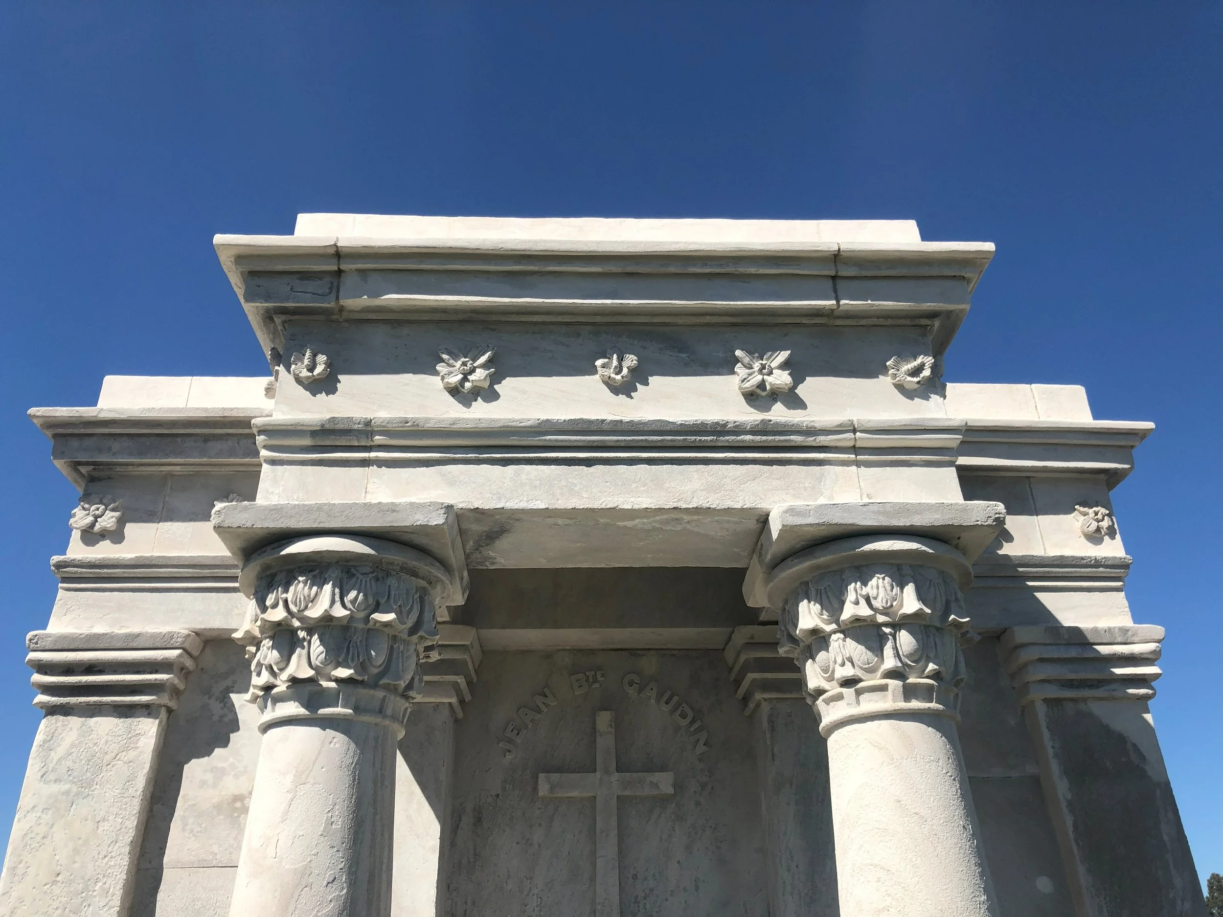 Close-up of a marble arch with decorated columns and inscriptions under a clear blue sky.
