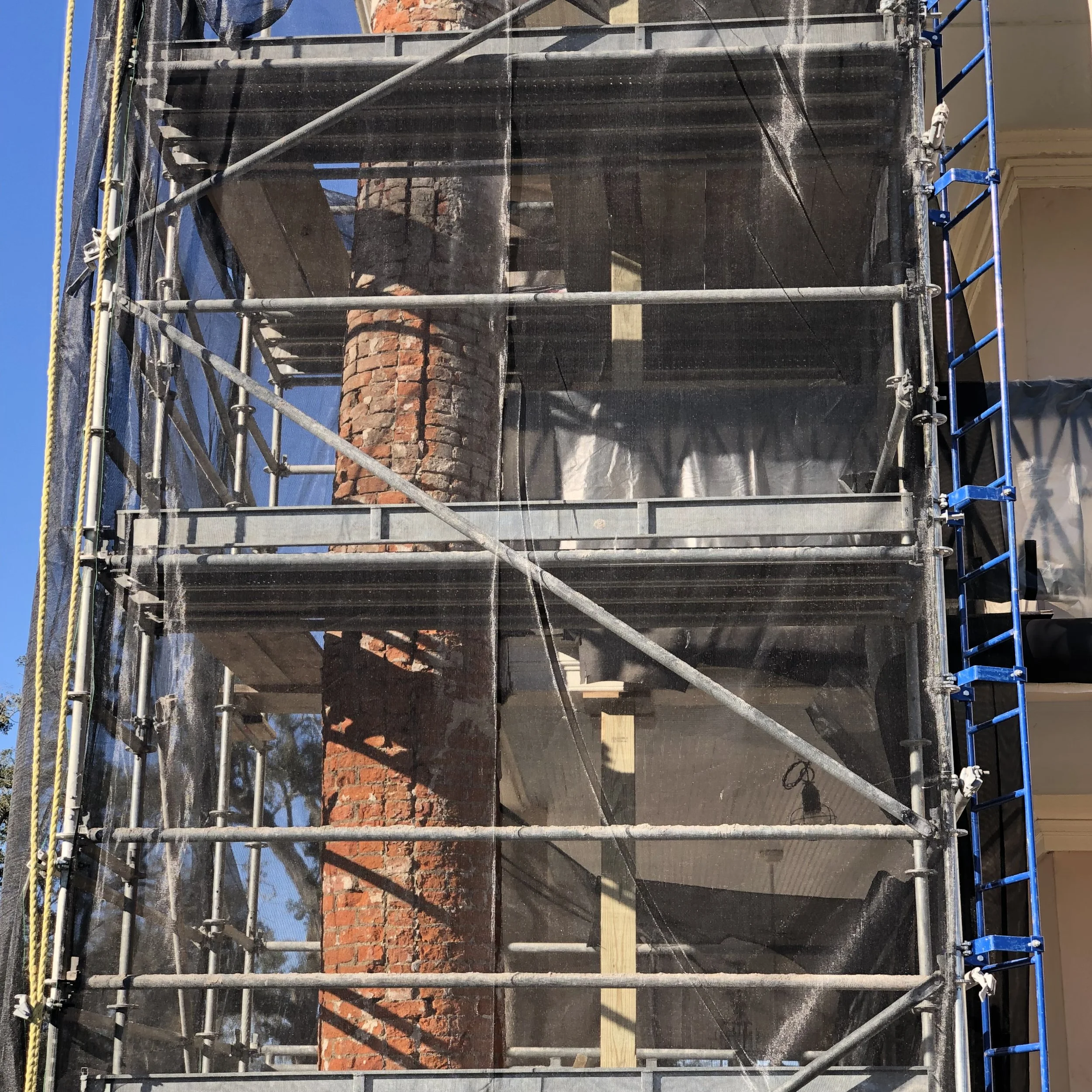 Construction scaffolding surrounding a brick chimney on a building.