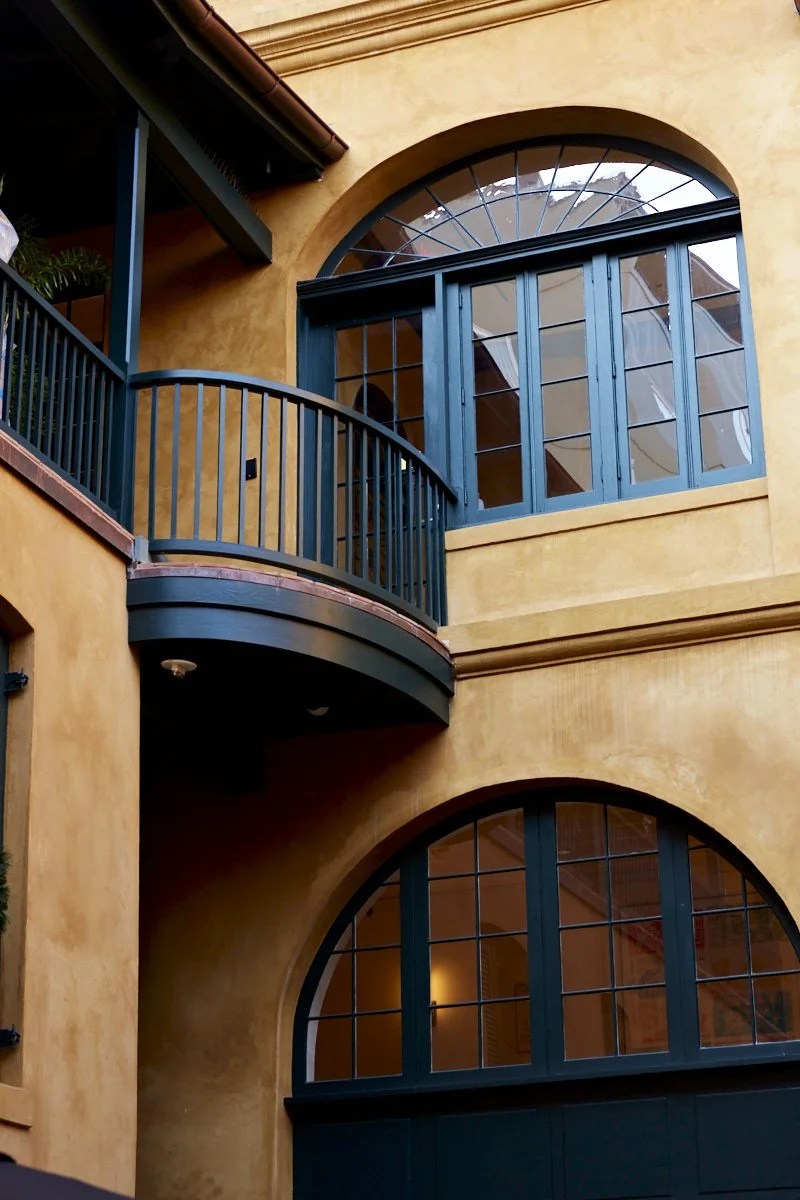 View of a Mediterranean-style building with yellow stucco walls, arched windows, and a black balcony railing. Exterior stucco restoration New Orleans
