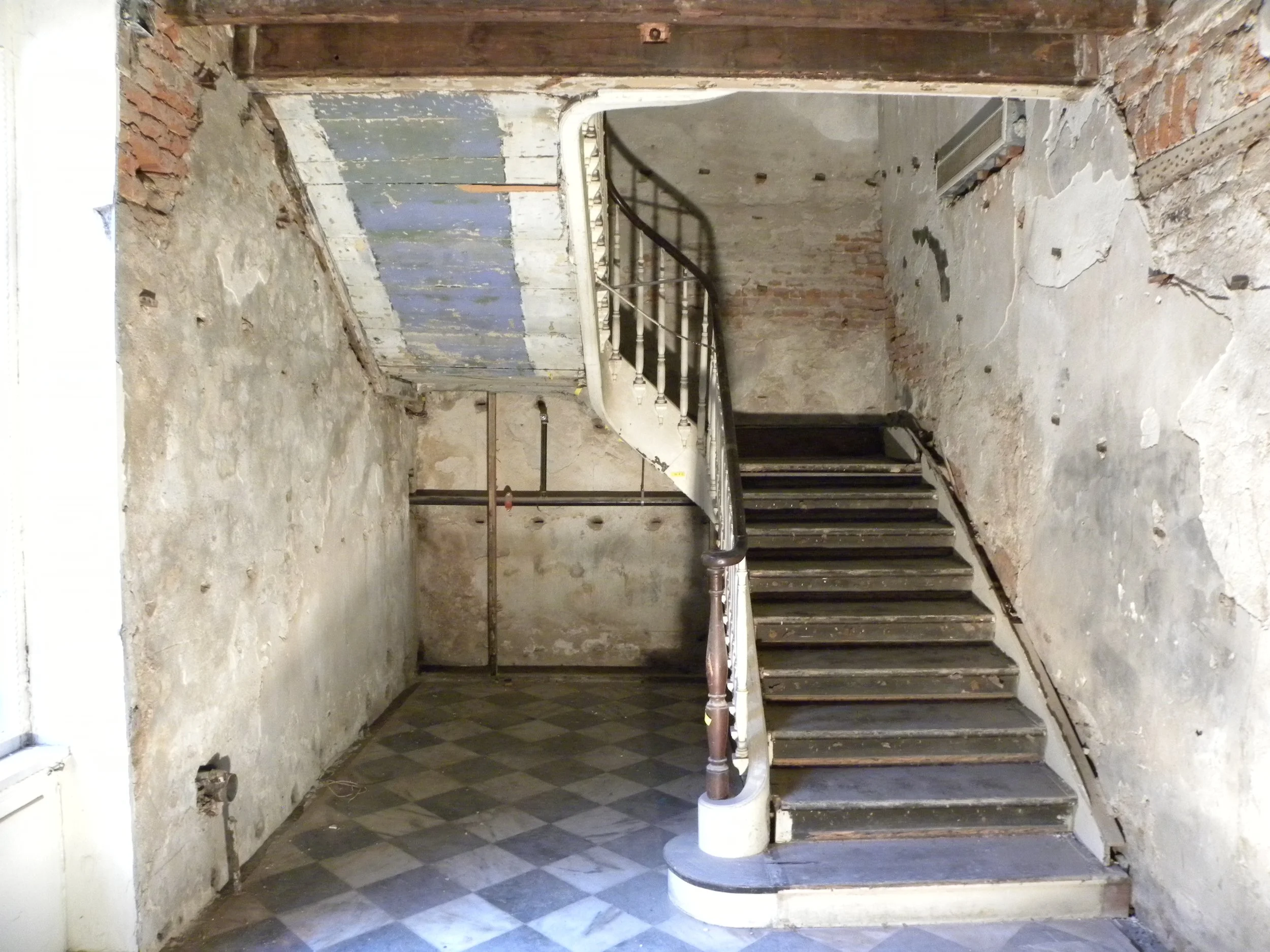 Old, worn staircase with peeling paint and exposed brick walls in a run-down interior space.