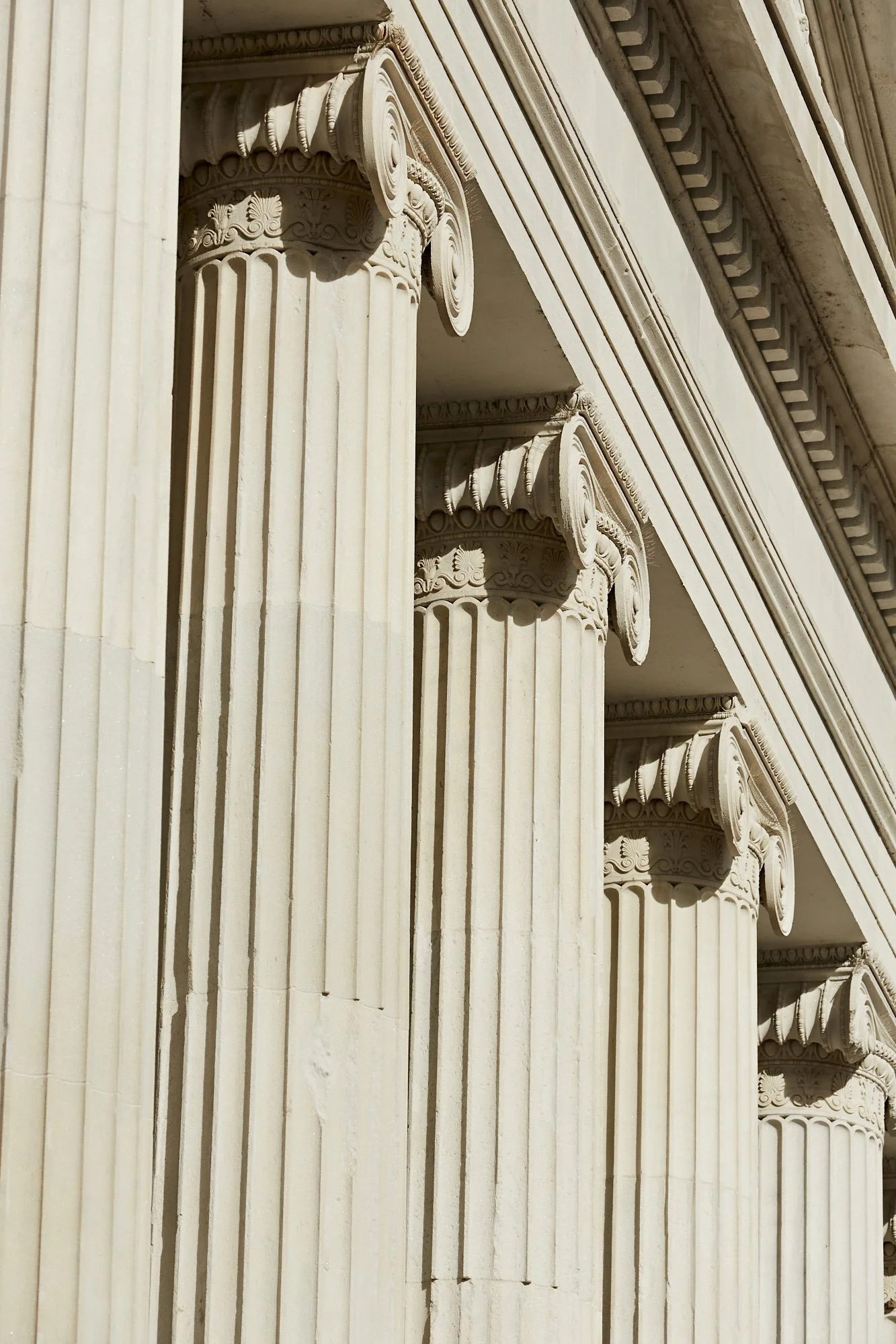 Close-up of classical architectural columns with ornate capitals, part of a building's exterior, in cream-colored stone.