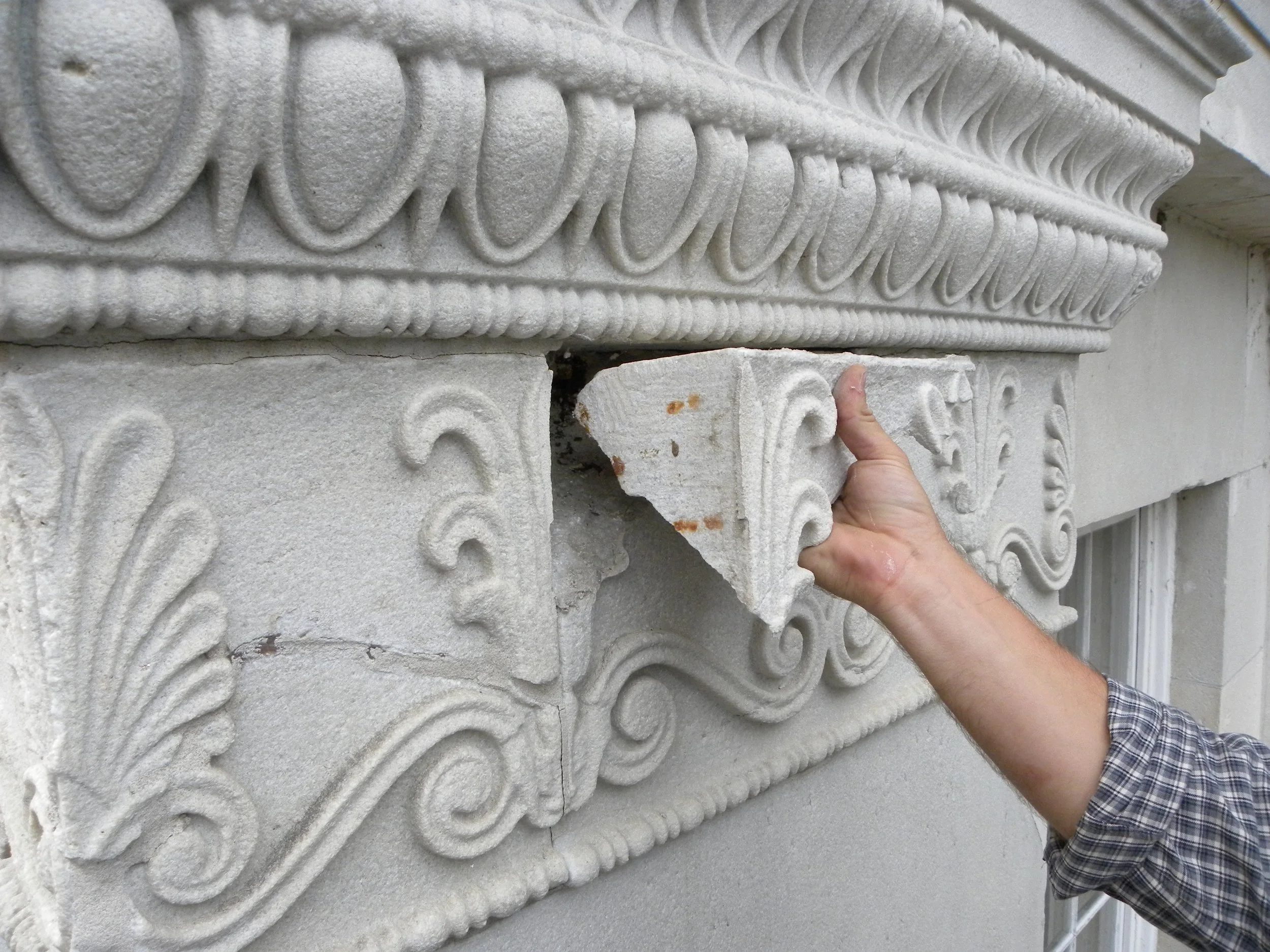Person installing decorative stone architectural element on building facade