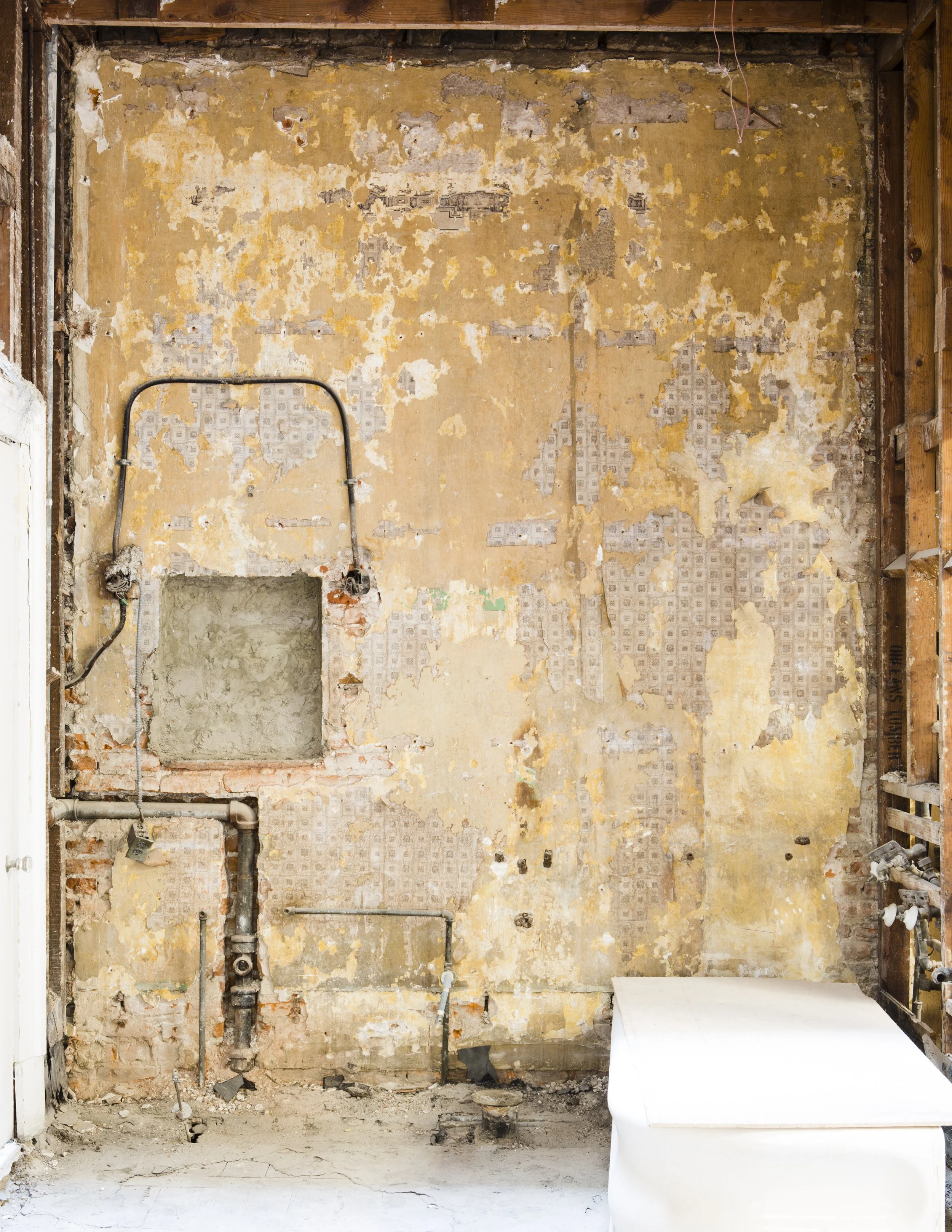 A partially renovated bathroom with exposed wall and plumbing, an empty space for a fixture, and a small white piece of furniture or countertop in the lower right corner.