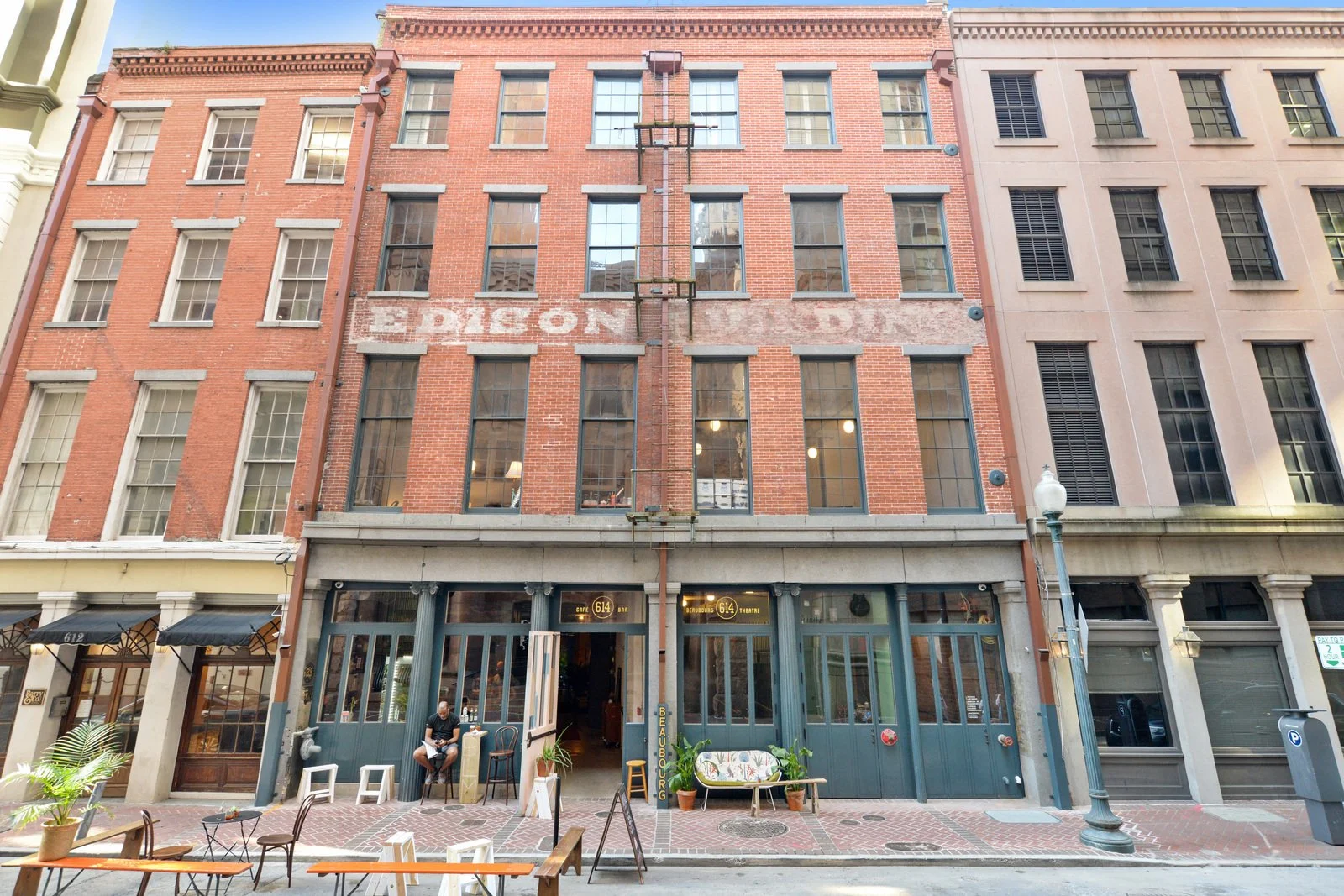 Street view with a brick building featuring painted signage, outdoor seating, a man sitting outside, and a lamppost. New Orleans historic architecture. Historic masonry restoration New Orleans. Brick repointing New Orleans. Brick cleaning.