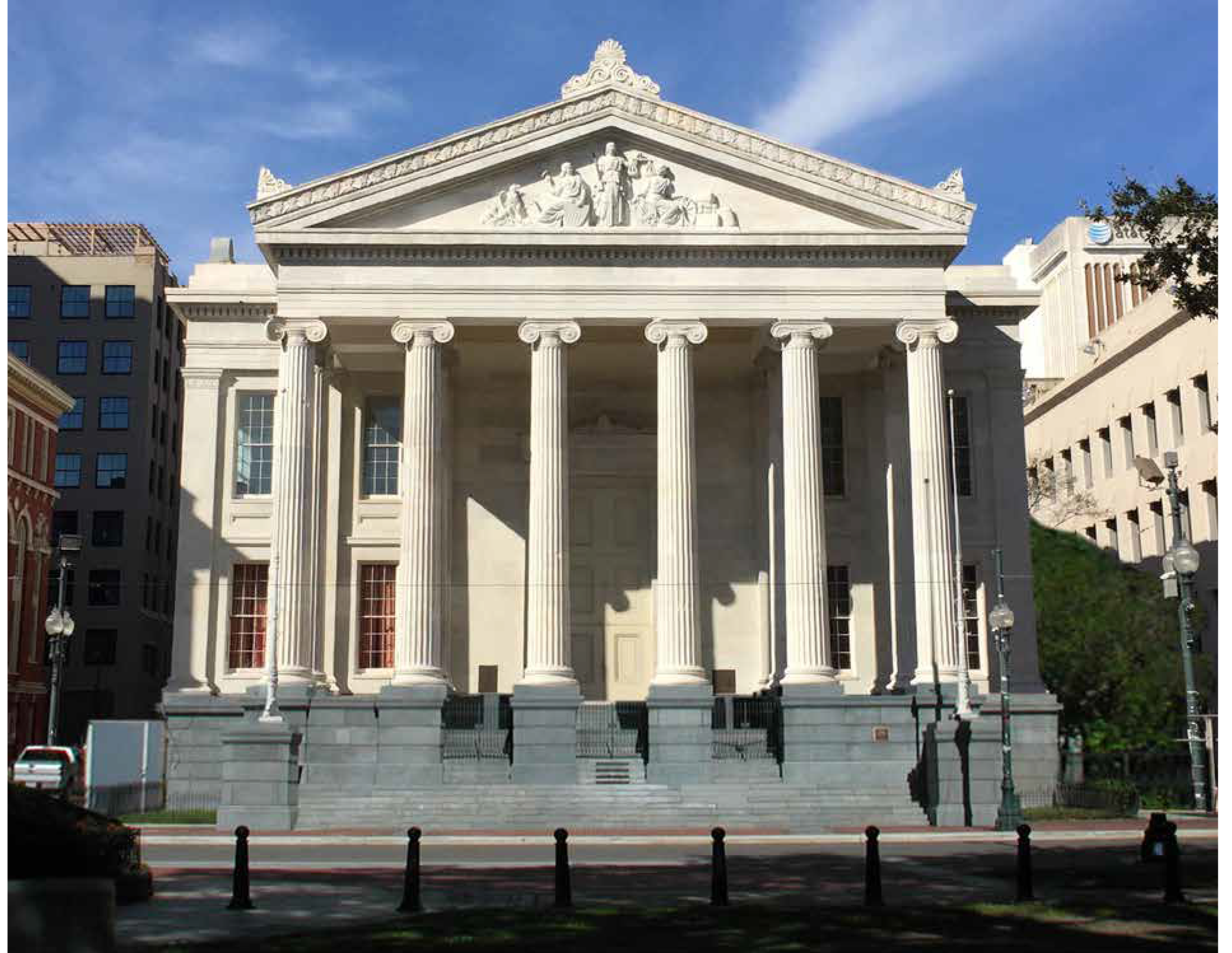 Front view of a classical-style white building with six tall columns, steps leading up to the entrance, and a triangular pediment with sculptures, under a blue sky.
