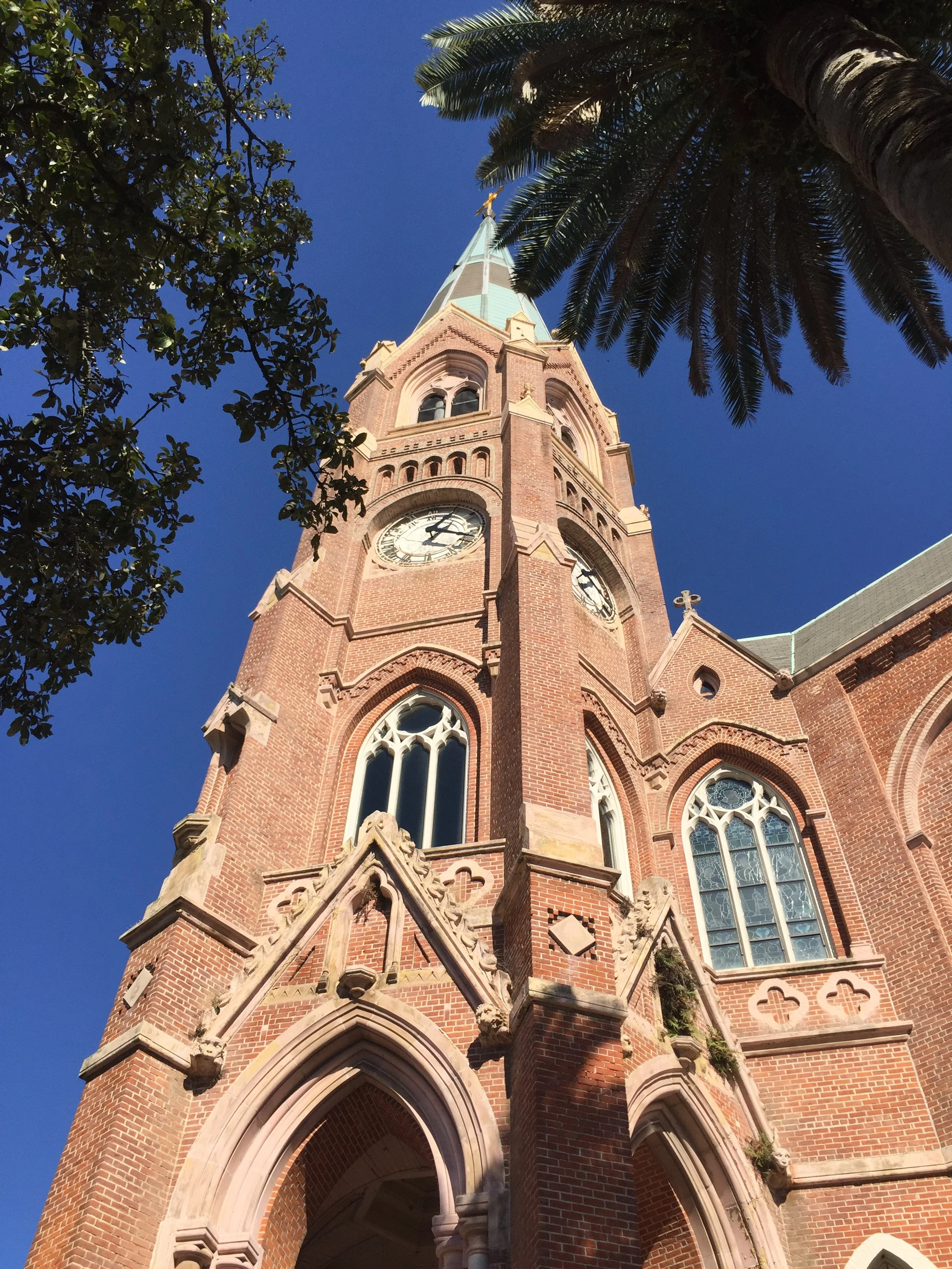 A tall brick church steeple with a clock, pointed roof, pointed arch windows, and ornate stone detailing. Historic stone restoration and repair. Masonry repair and restoration. Brick repointing, brick repair, brick restoration. Historic masonry 