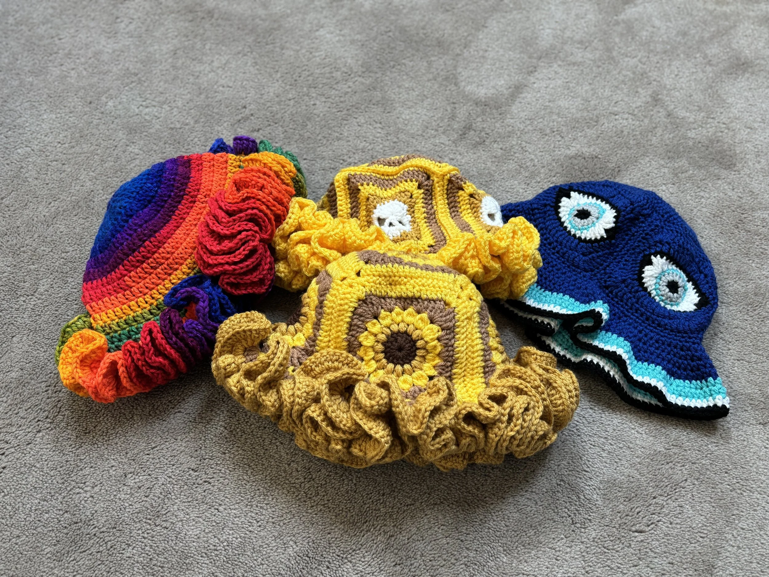 Colorful handmade crochet hats with ruffled brims, featuring various patterns and designs, placed on a gray surface.