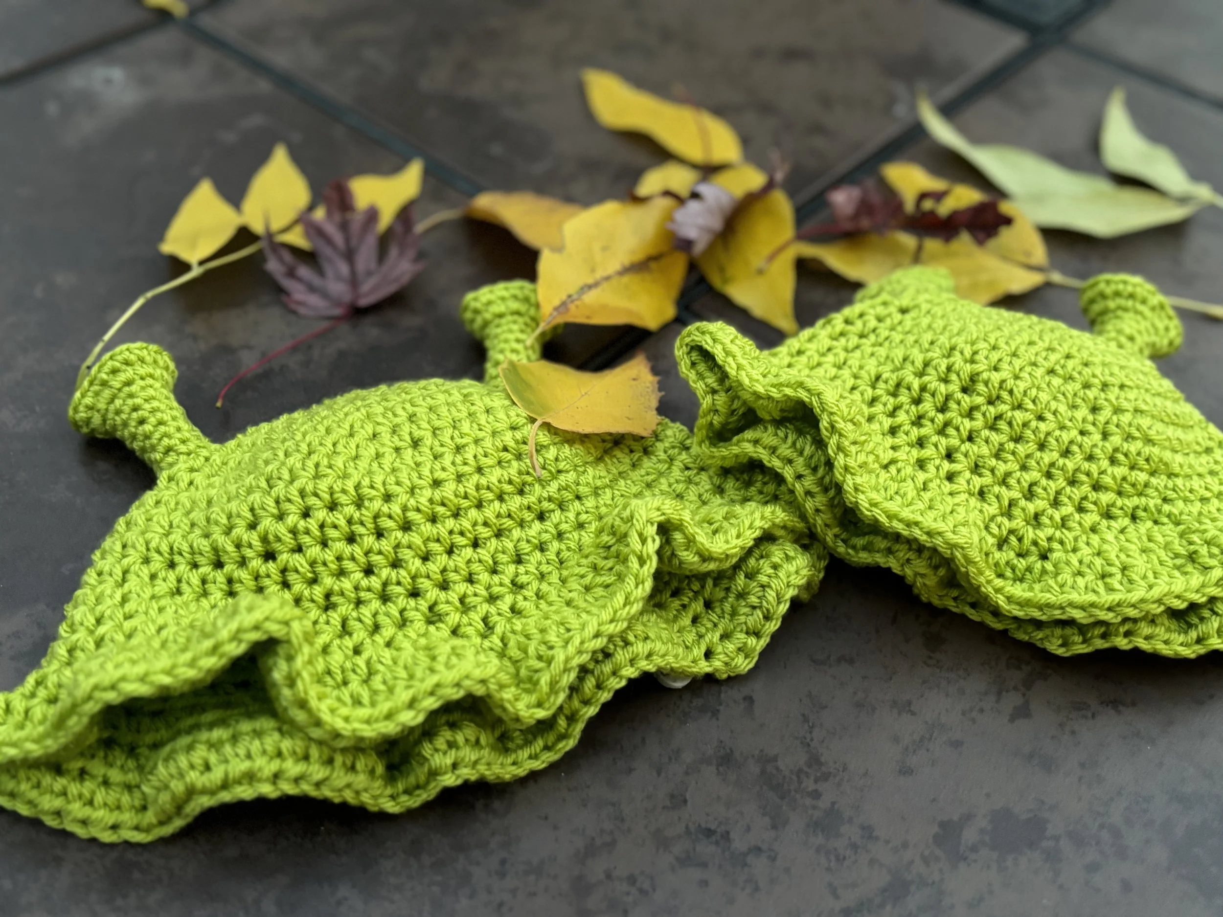Green crocheted bikini top with ruffled edges on a tile floor, surrounded by scattered yellow and brown leaves.