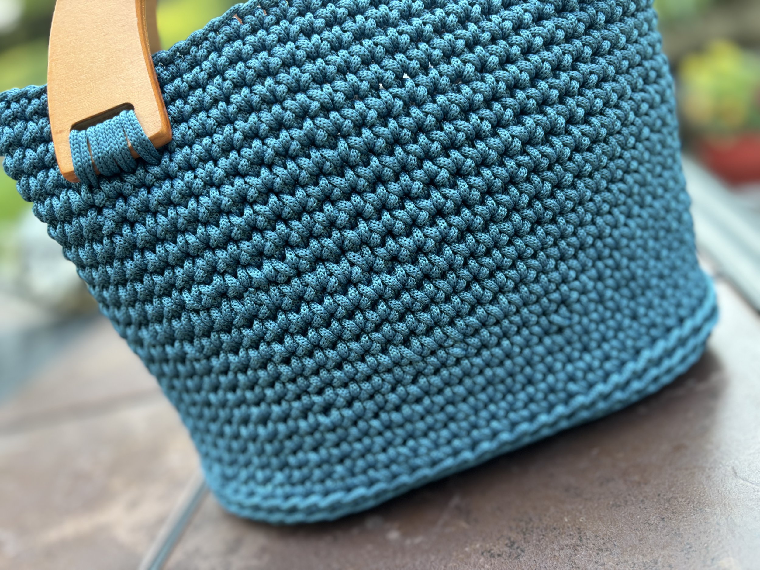 Close-up of a blue crochet bag with wooden handles on a table.