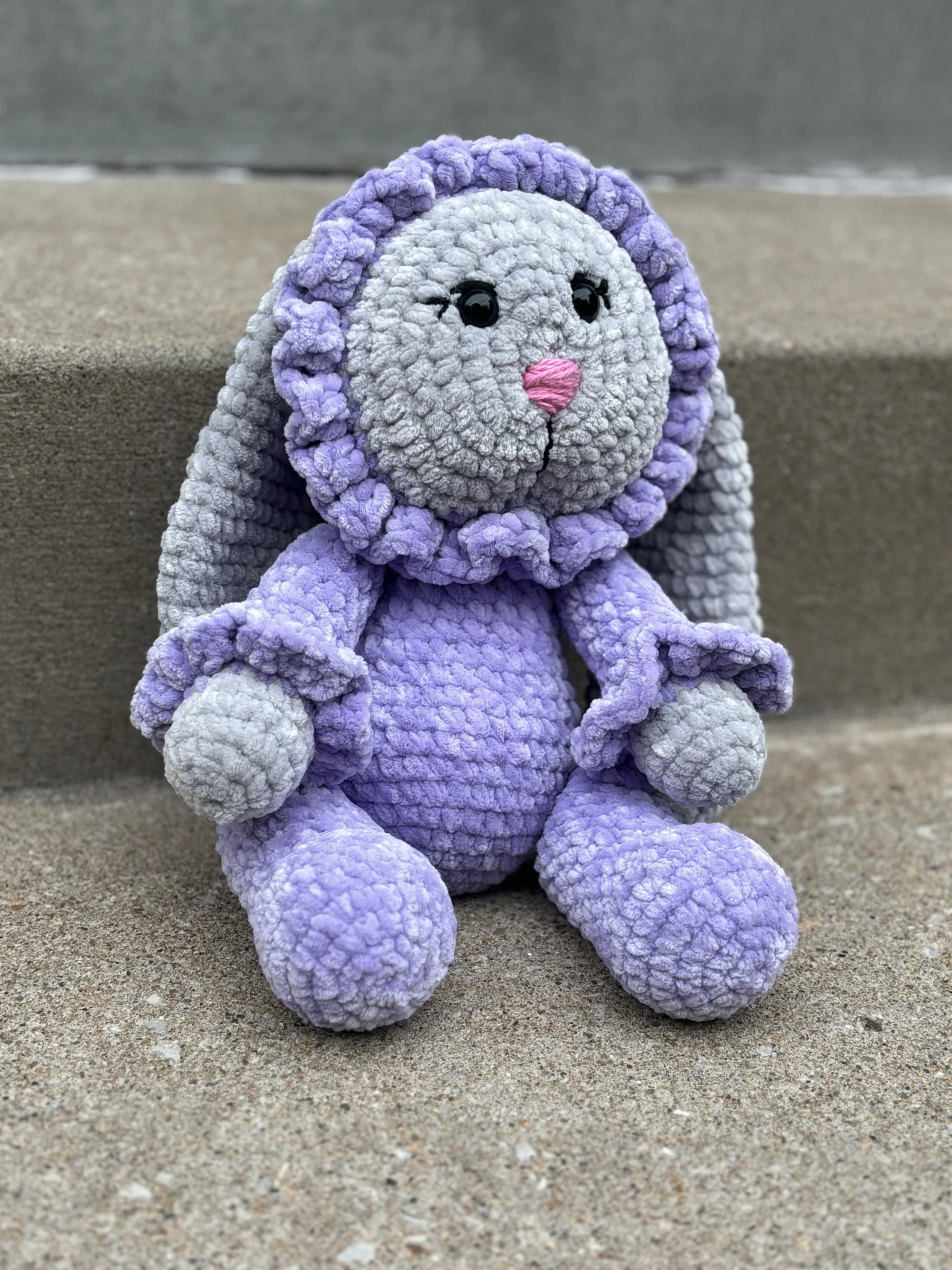 Knitted plush bunny toy with purple and gray textures on a concrete step.