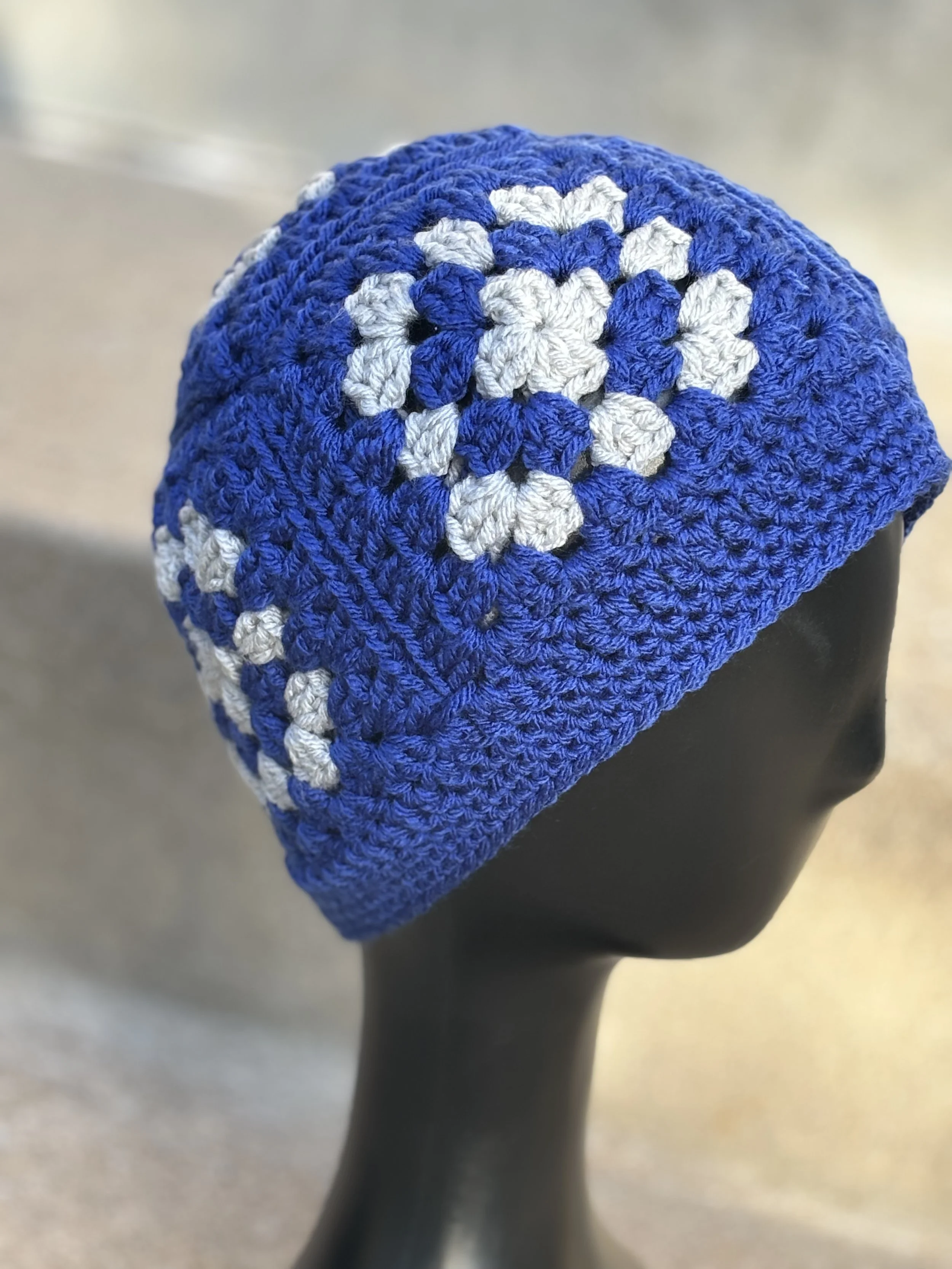 Blue crocheted hat with white flower patterns on a mannequin head.