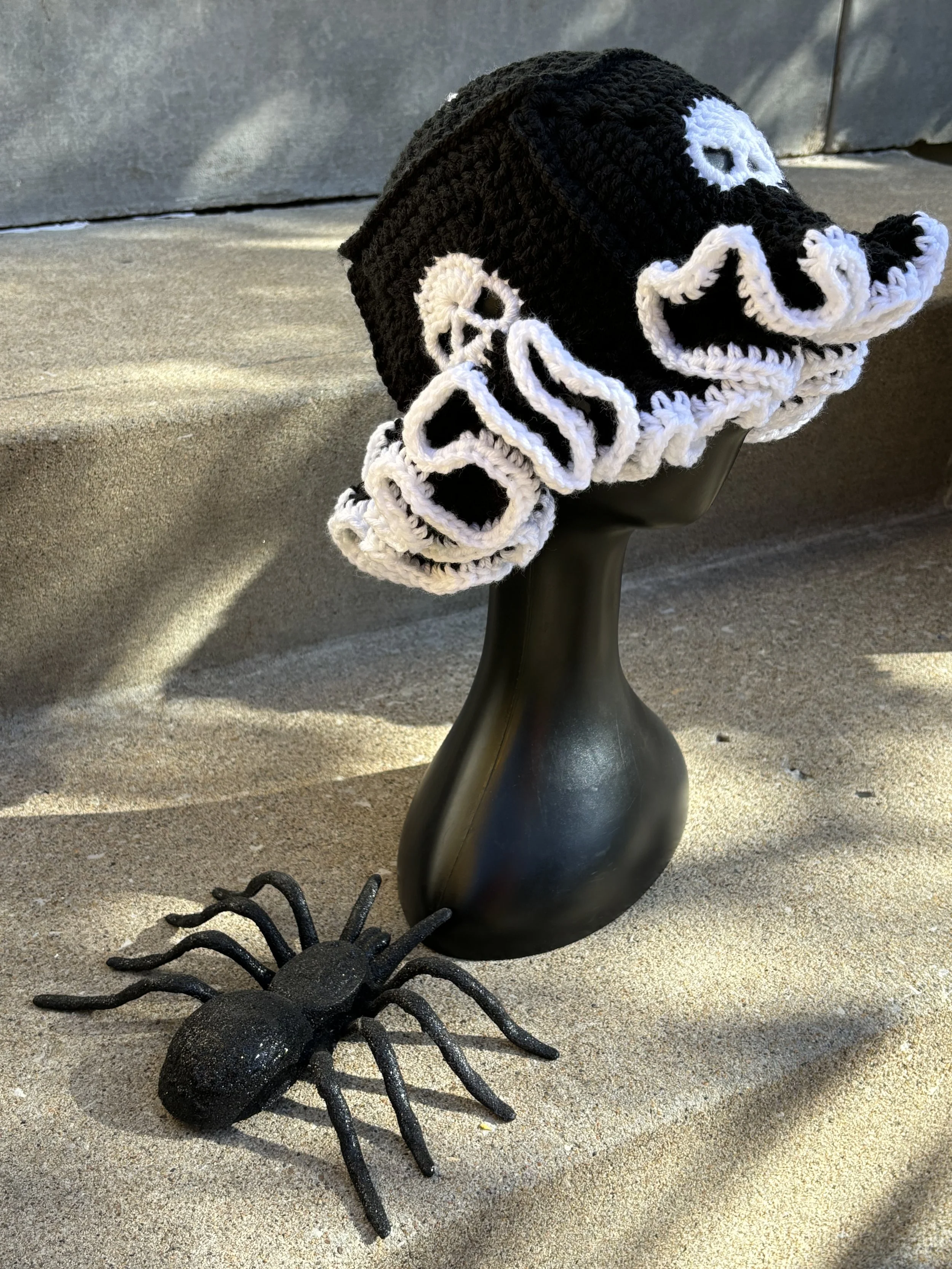 Black and white crocheted hat on mannequin head with decorative spider