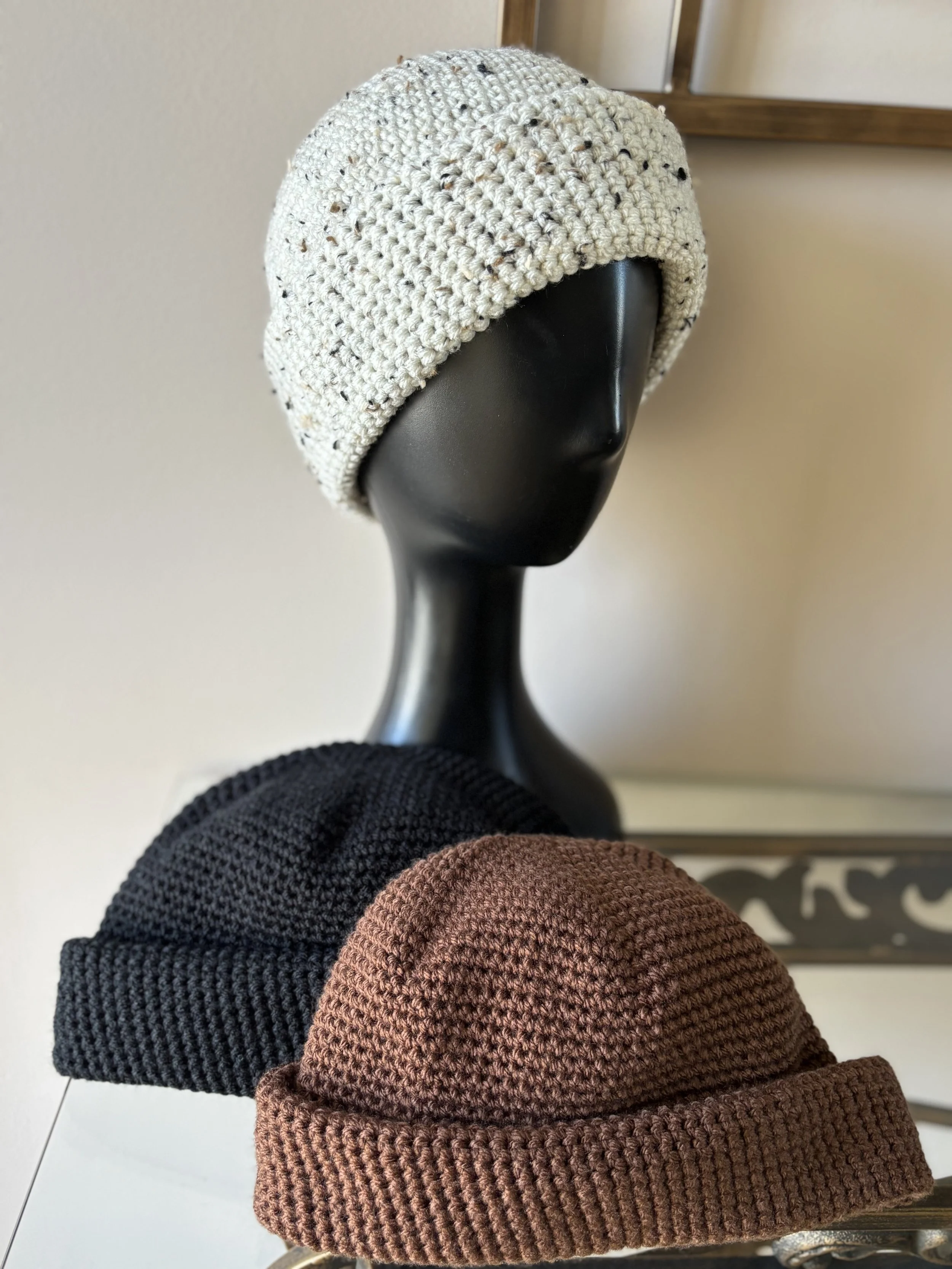 Knitted hats in white, black, and brown displayed on a mannequin.