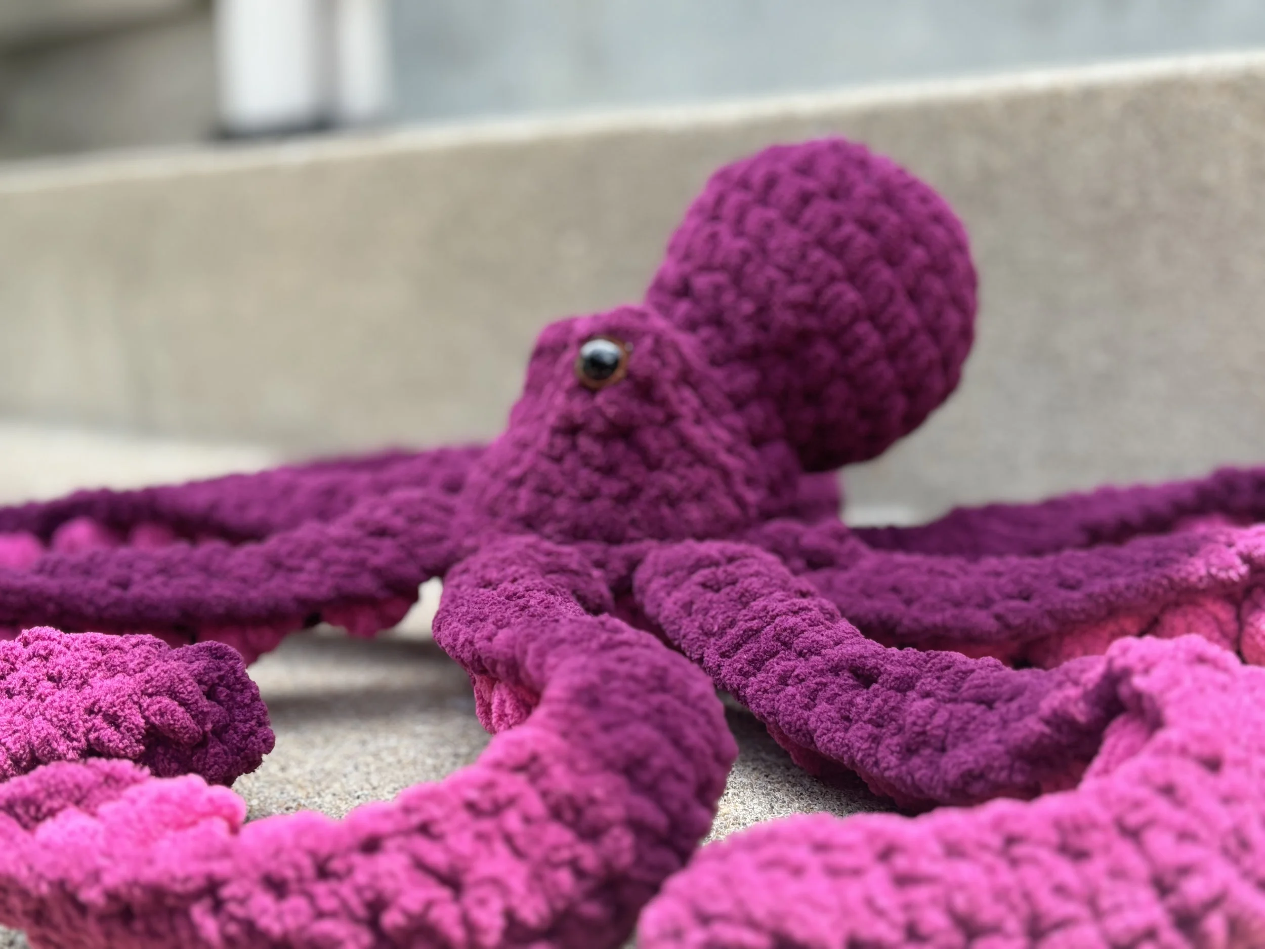 Crocheted purple octopus plush toy on a concrete surface