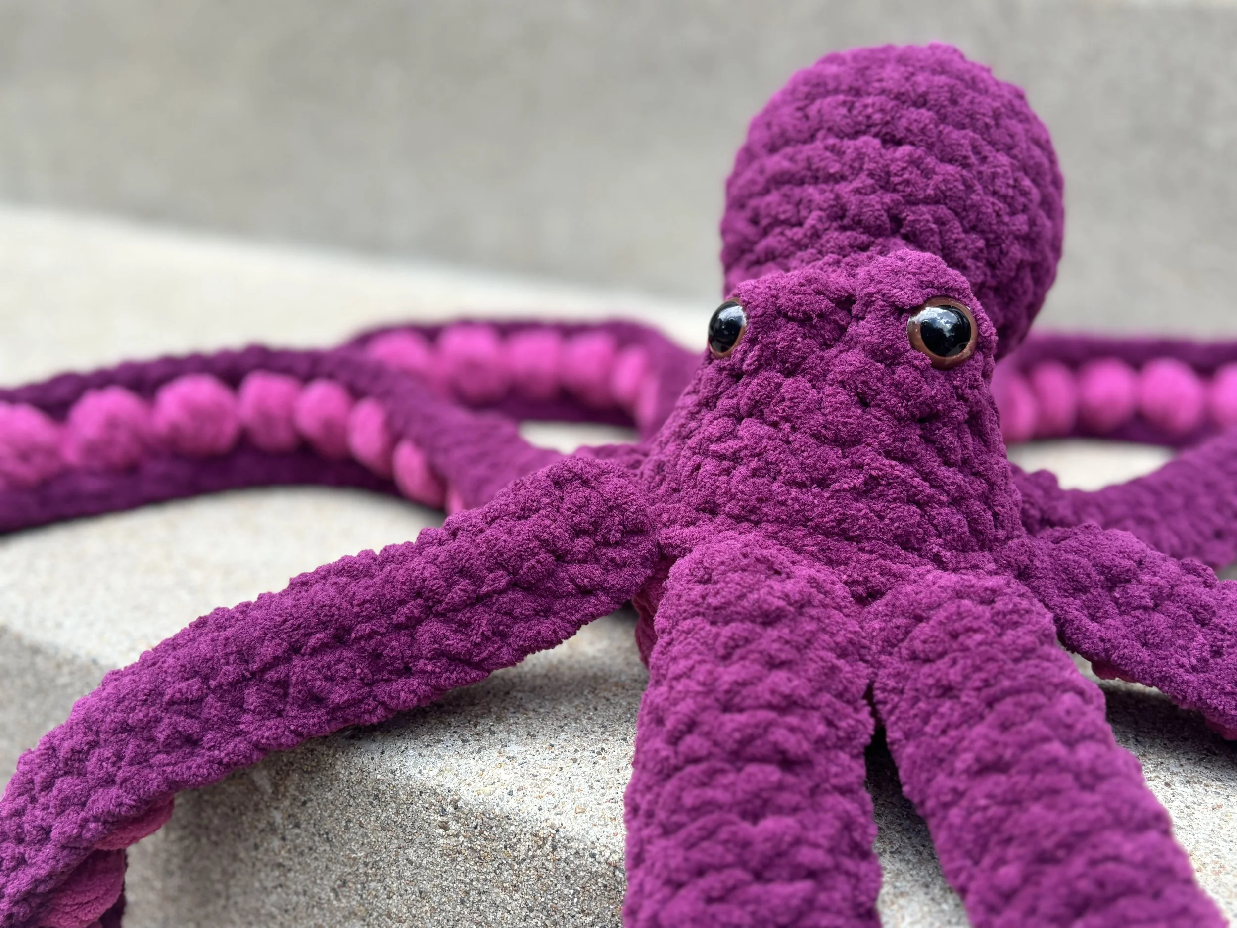 Plush purple octopus toy with textured fabric and button eyes on a gray surface.
