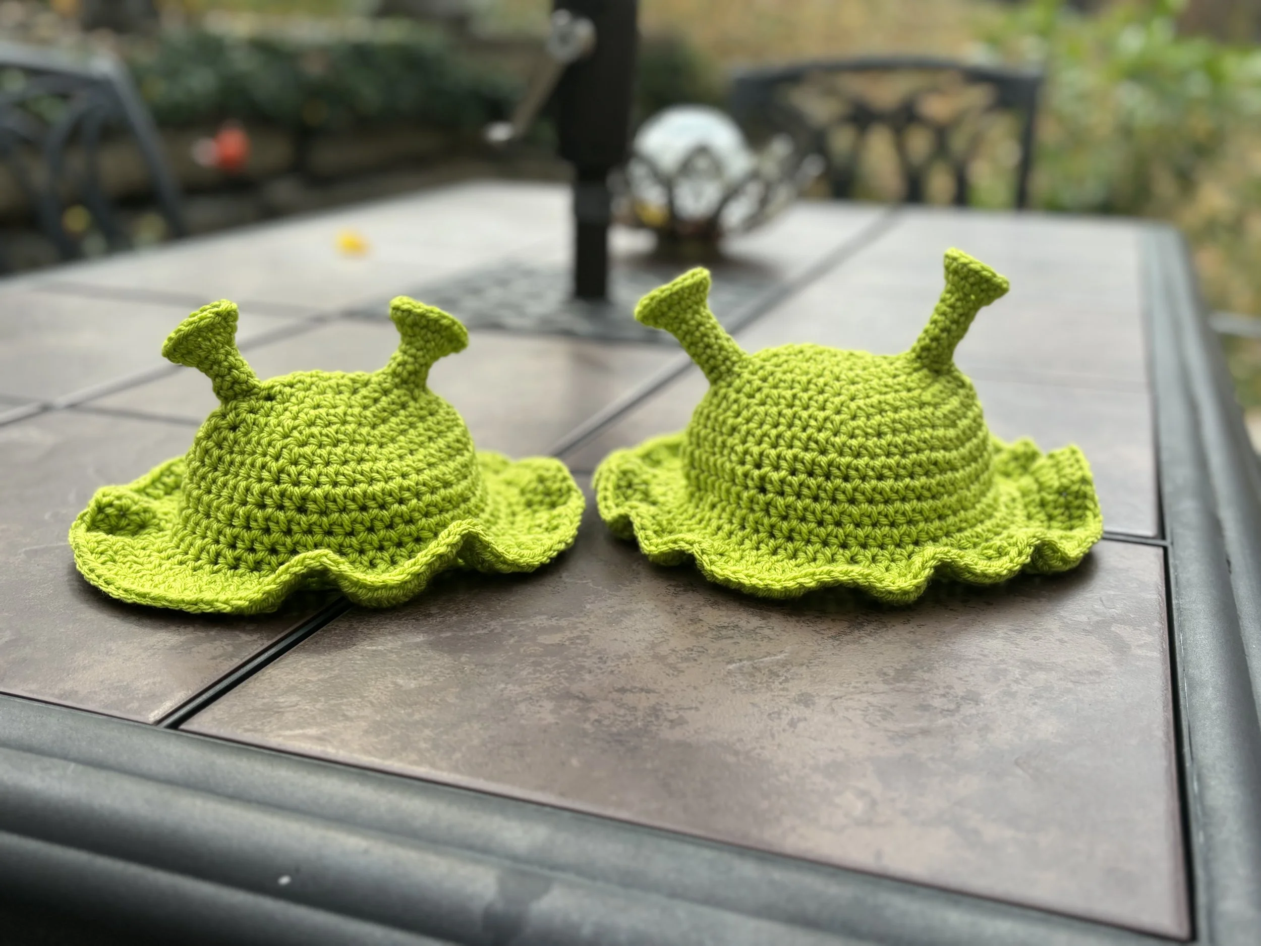Two green crochet hats with spiral antennas on a table.