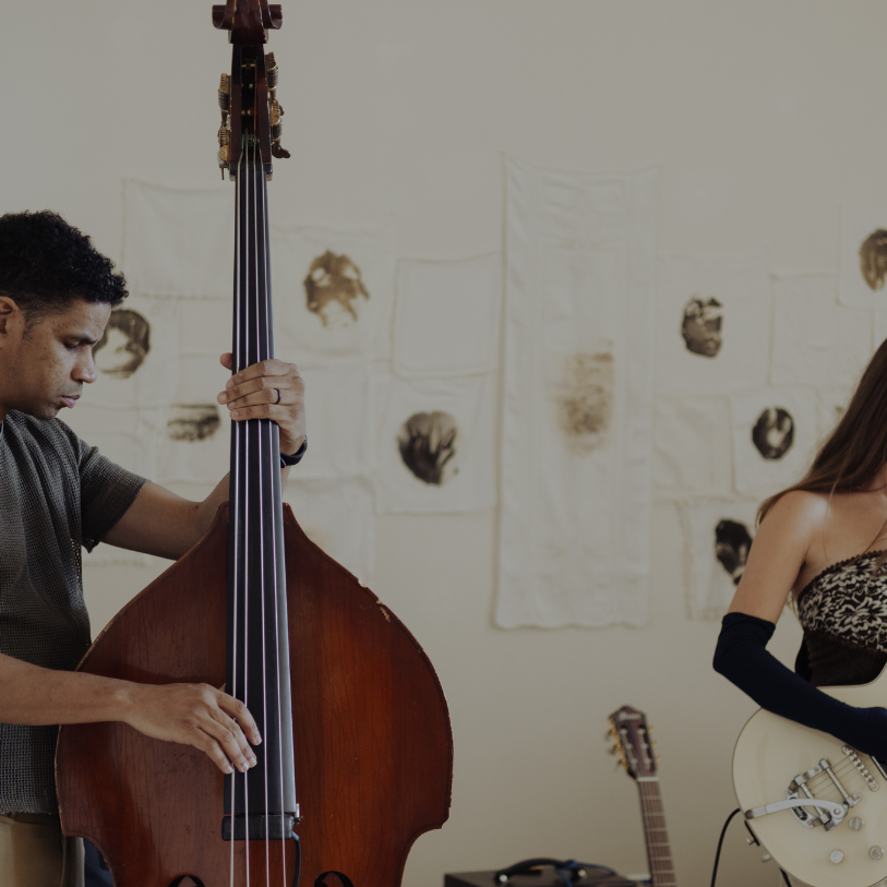 Musicians playing a double bass and an electric guitar in a room with artwork on the wall.