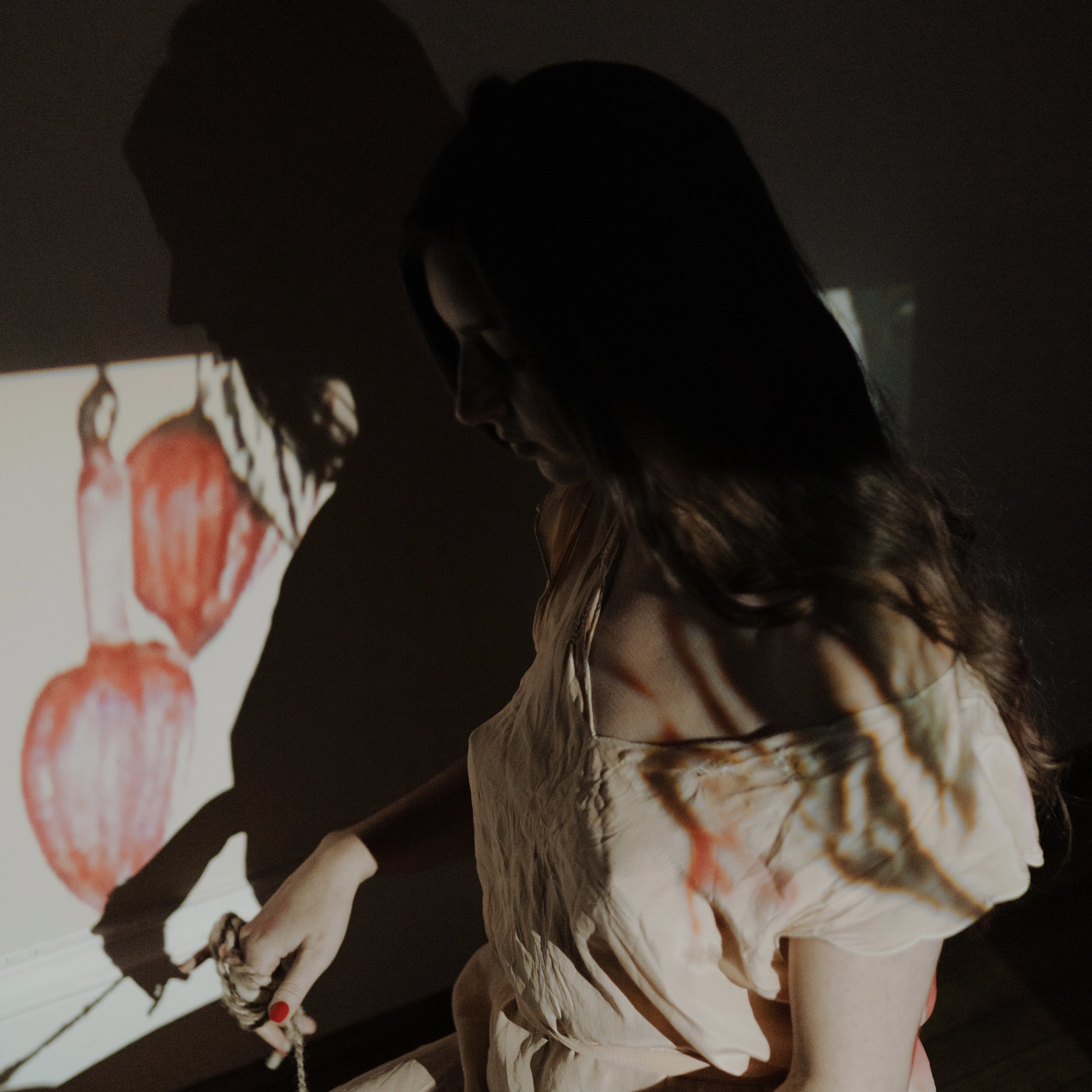 A woman with long dark hair looks down as colorful abstract art is projected onto her and the wall behind her.