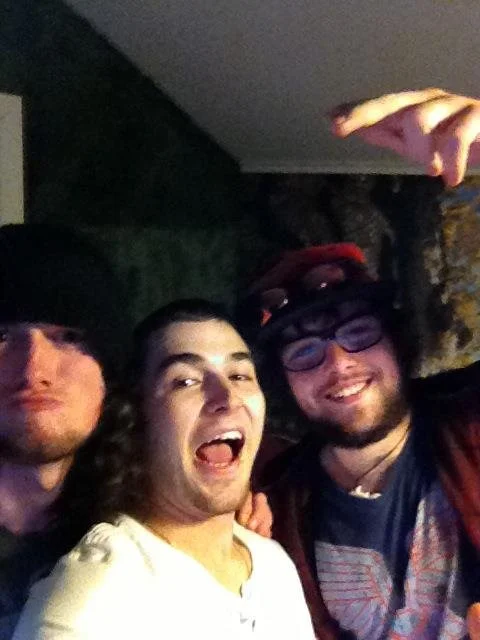 Three young men taking a selfie outdoors at night, smiling and making fun expressions.