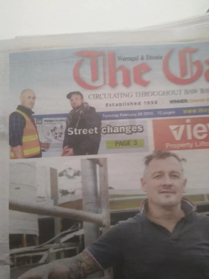 A newspaper that features photos of two men, one in a safety vest and the other wearing a jacket, with a headline about street changes and other advertisements in the background.