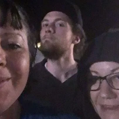 Three people taking a selfie together, smiling and looking at the camera, in a dark setting.