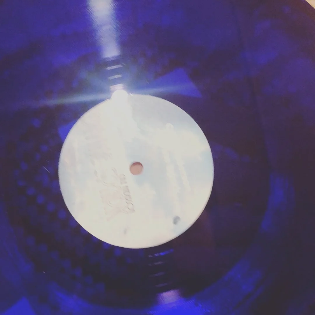 Close-up of a vinyl record with a white label in the center, illuminated by a light source reflected on the surface.