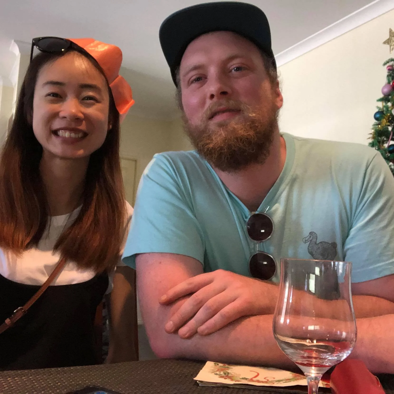 A smiling woman with glasses on her head and a man with a beard and cap posing together at a table.