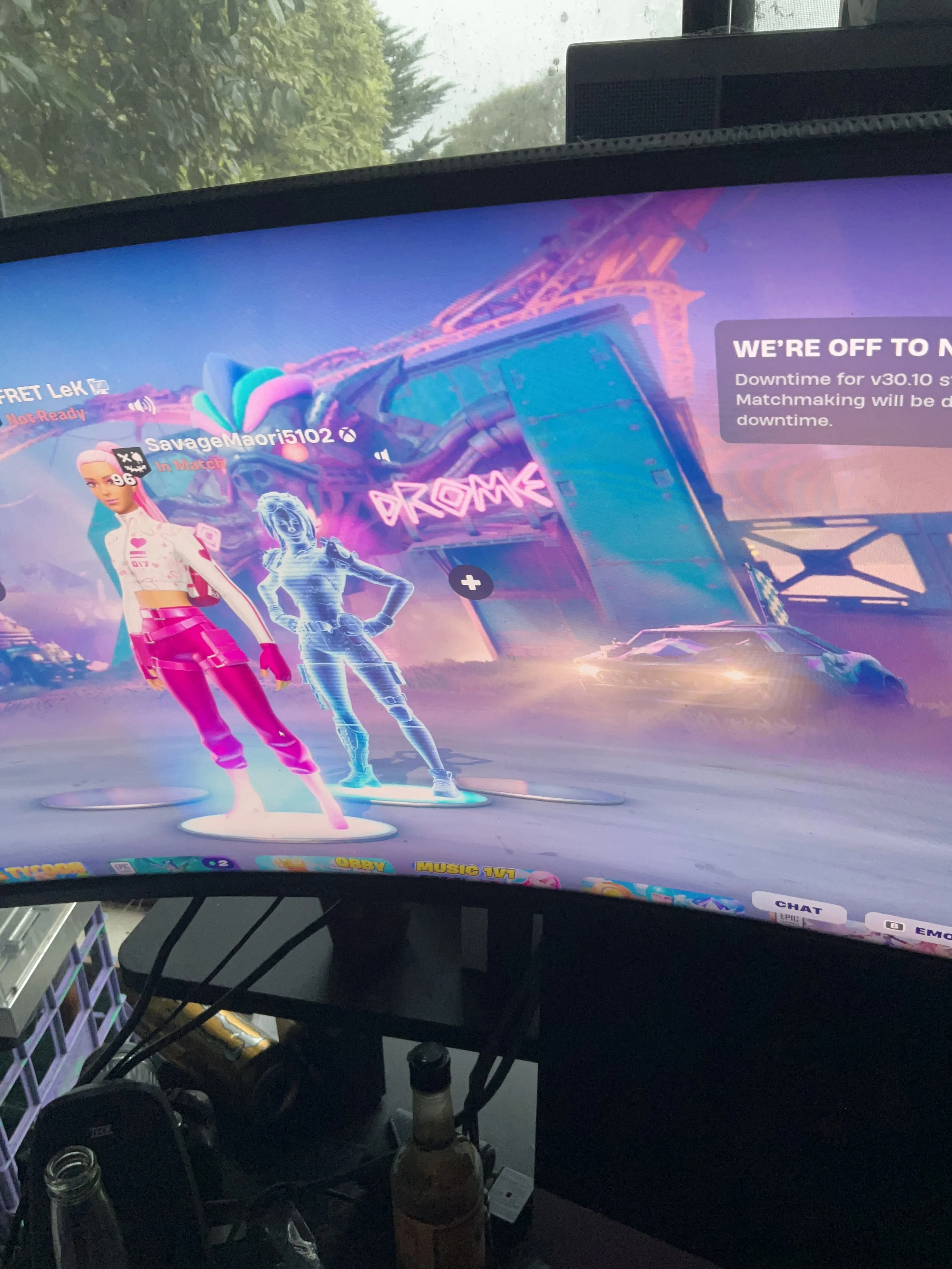 A computer monitor displaying the Fortnite game with characters in futuristic outfits, set in a neon-lit environment outside a nightclub or amusement park, with a message indicating the game servers are off-line.