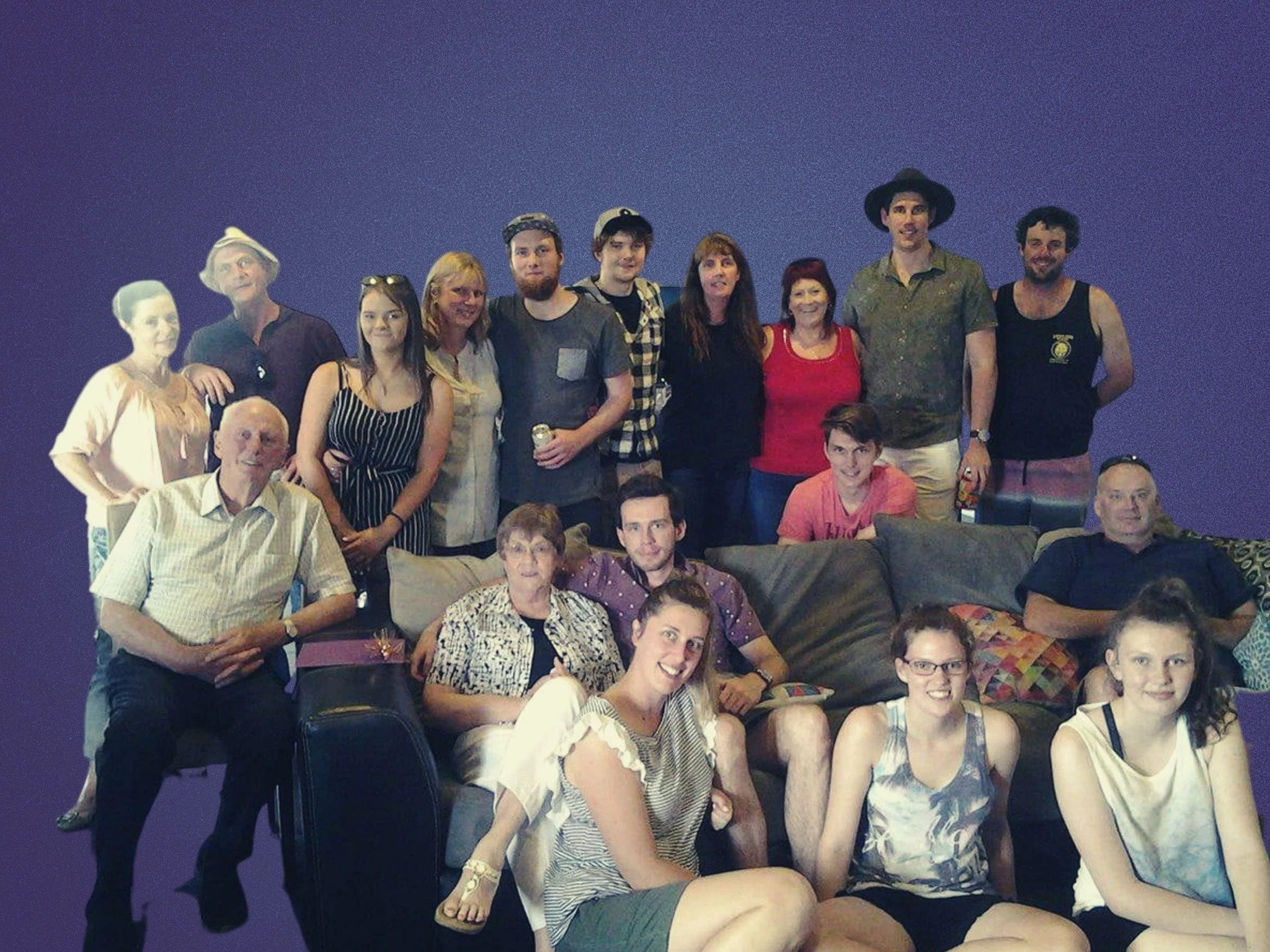 Group of fifteen people, with some sitting on a sofa and some standing behind, posing for a photo in front of a plain purple background.