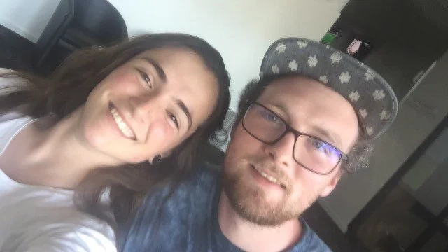 A woman and a man taking a selfie together indoors, smiling at the camera.