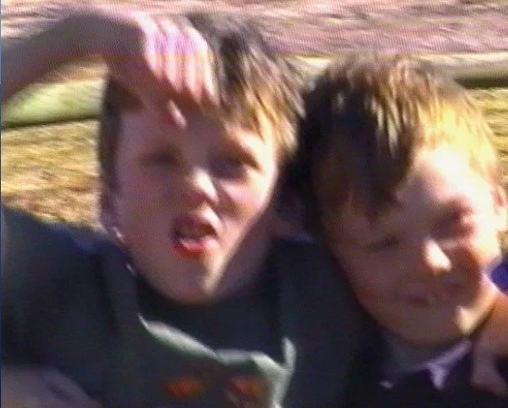 Two boys with messy hair and expressive faces, standing outdoors, possibly posing for a photo.