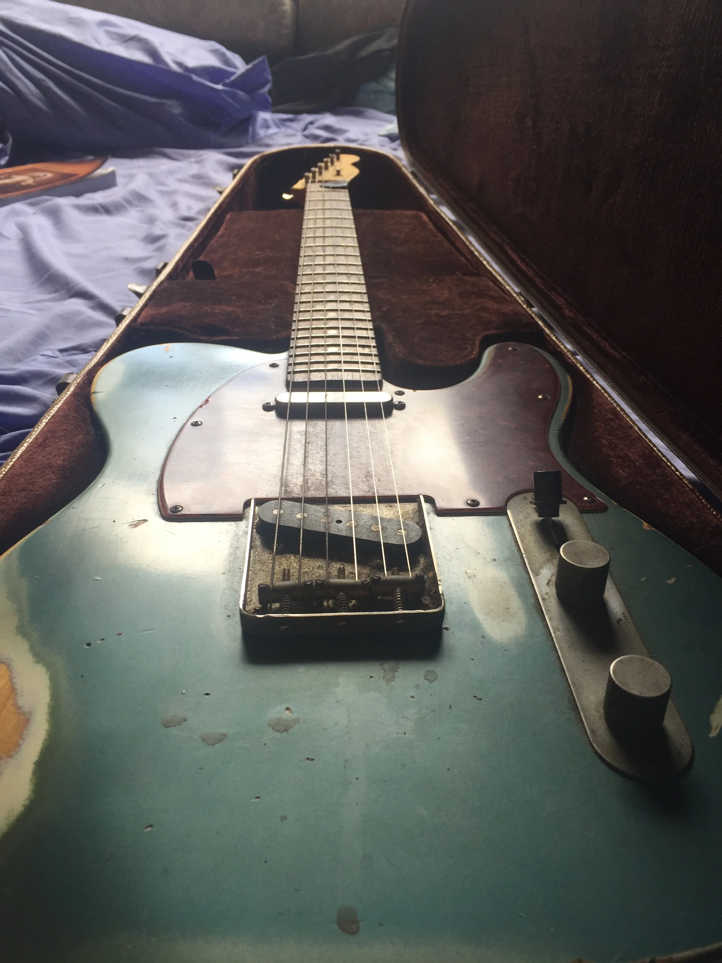 An old electric guitar with a worn, chipped blue paint job inside a brown case.