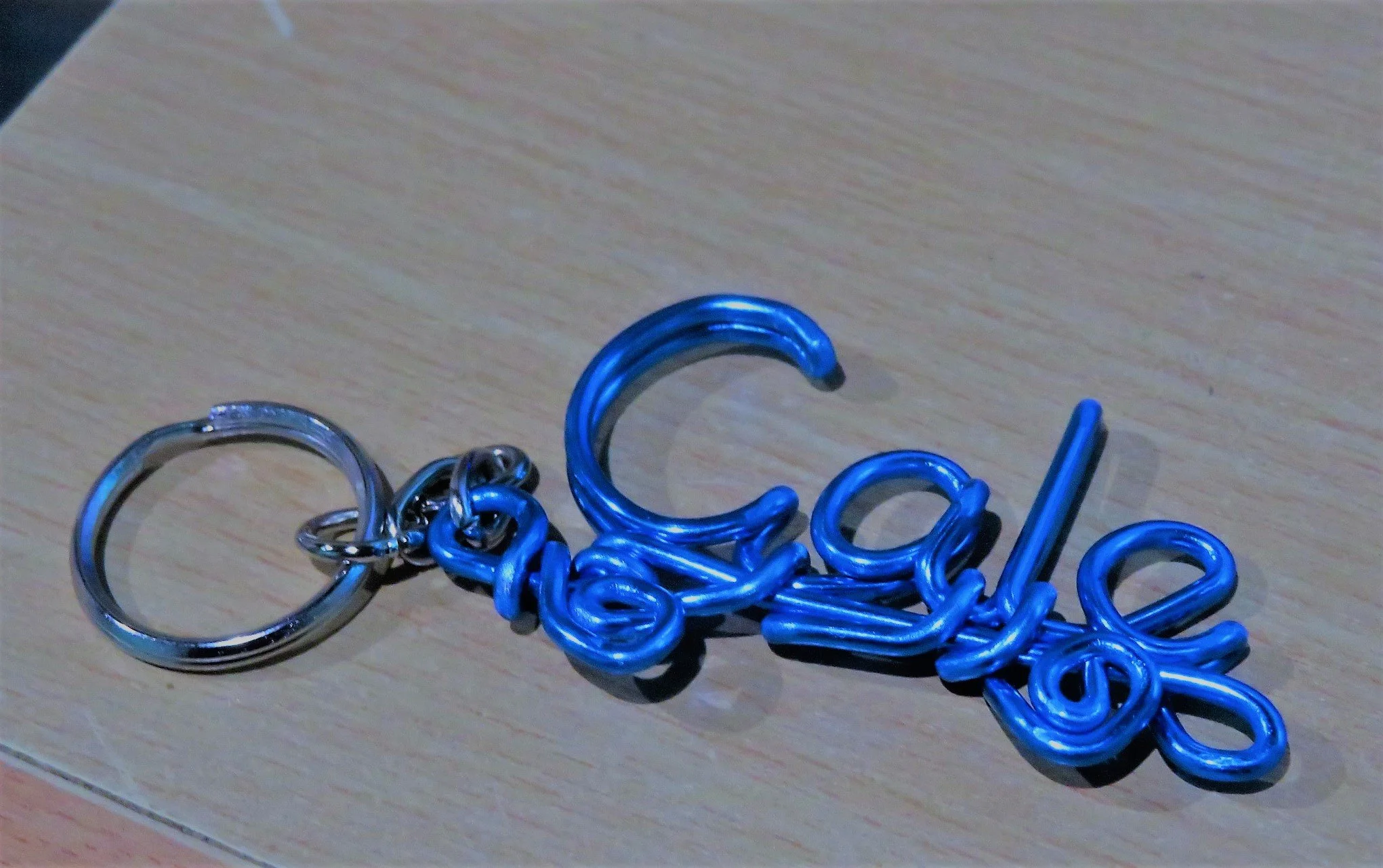 Keychain with the word 'School' crafted from blue wire laying on a wooden surface.