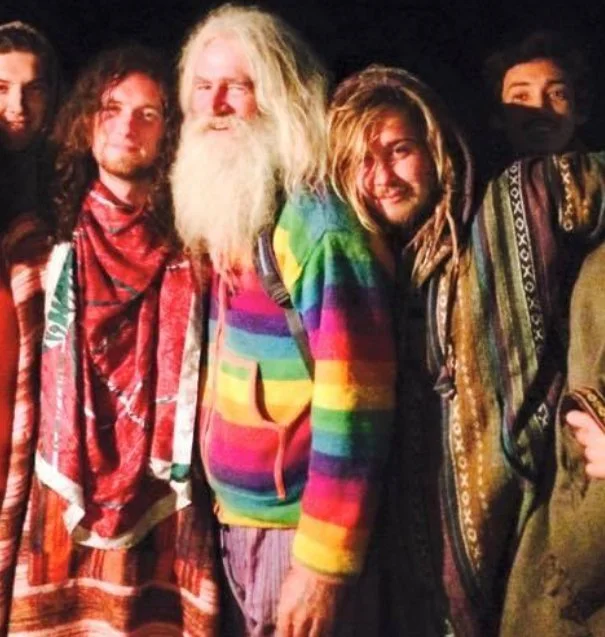 Group of five diverse people at night, wearing colorful and patterned clothing, smiling, standing outdoors.