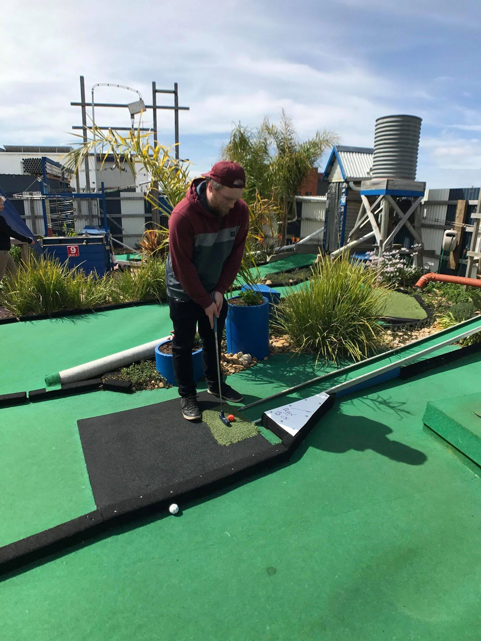 Man playing mini golf on an outdoor course with plants and structures around