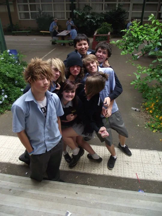Group of seven children standing outdoors in a school courtyard.