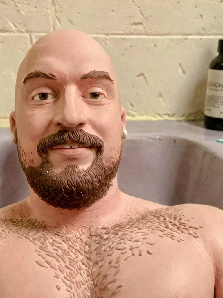 A man with a fake beard and eyebrows, smiling at the camera, sitting in a bathtub with a bottle of soap or shampoo in the background.