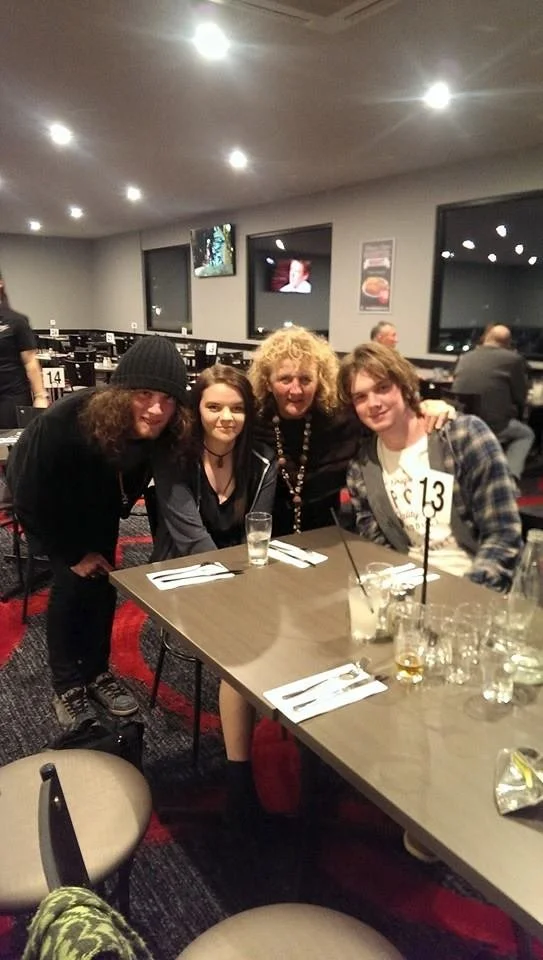 Four people sitting at a restaurant table, smiling for a photo. The table has drinks and utensils.