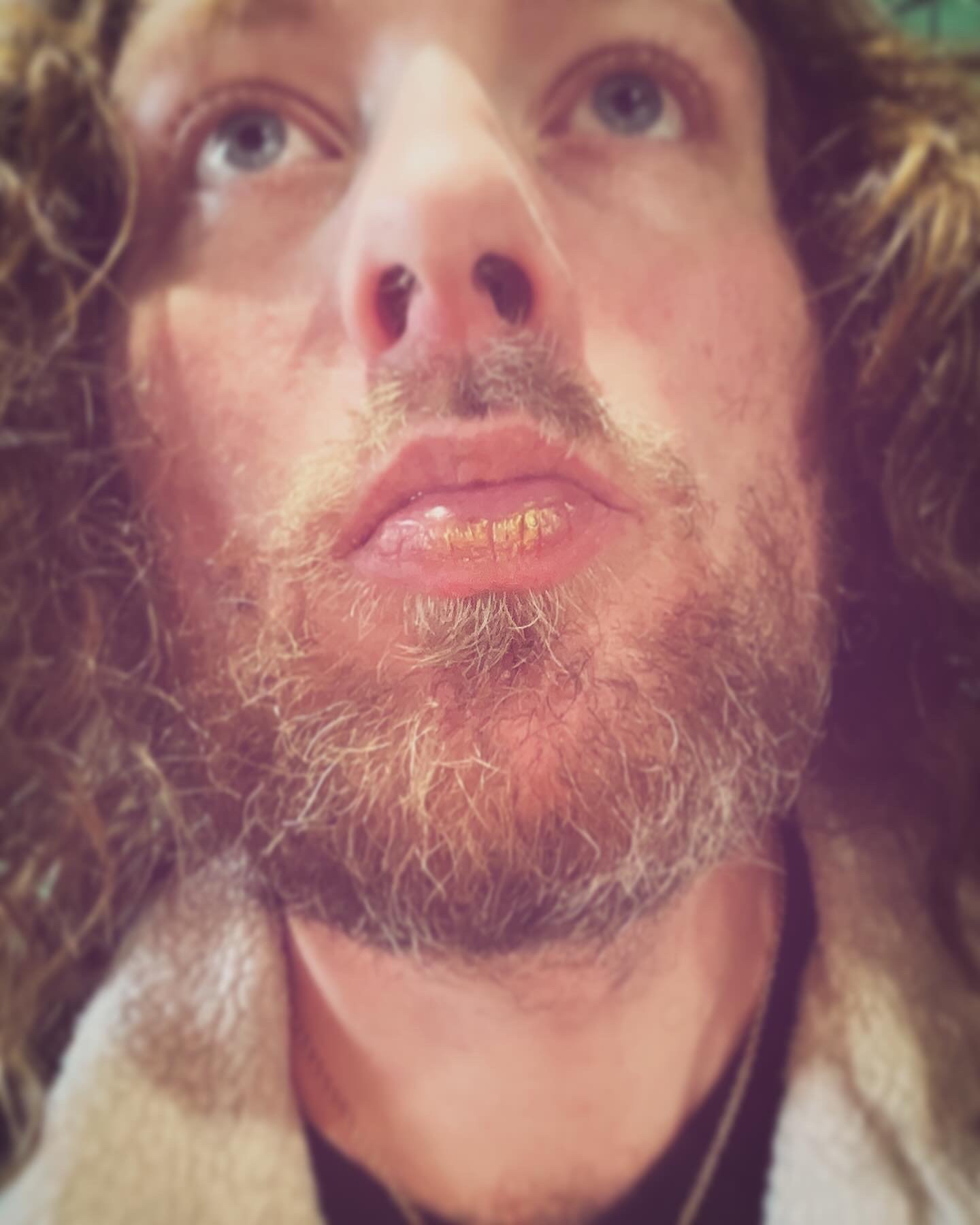 Close-up of a man's face with long curly hair and a beard, looking up.