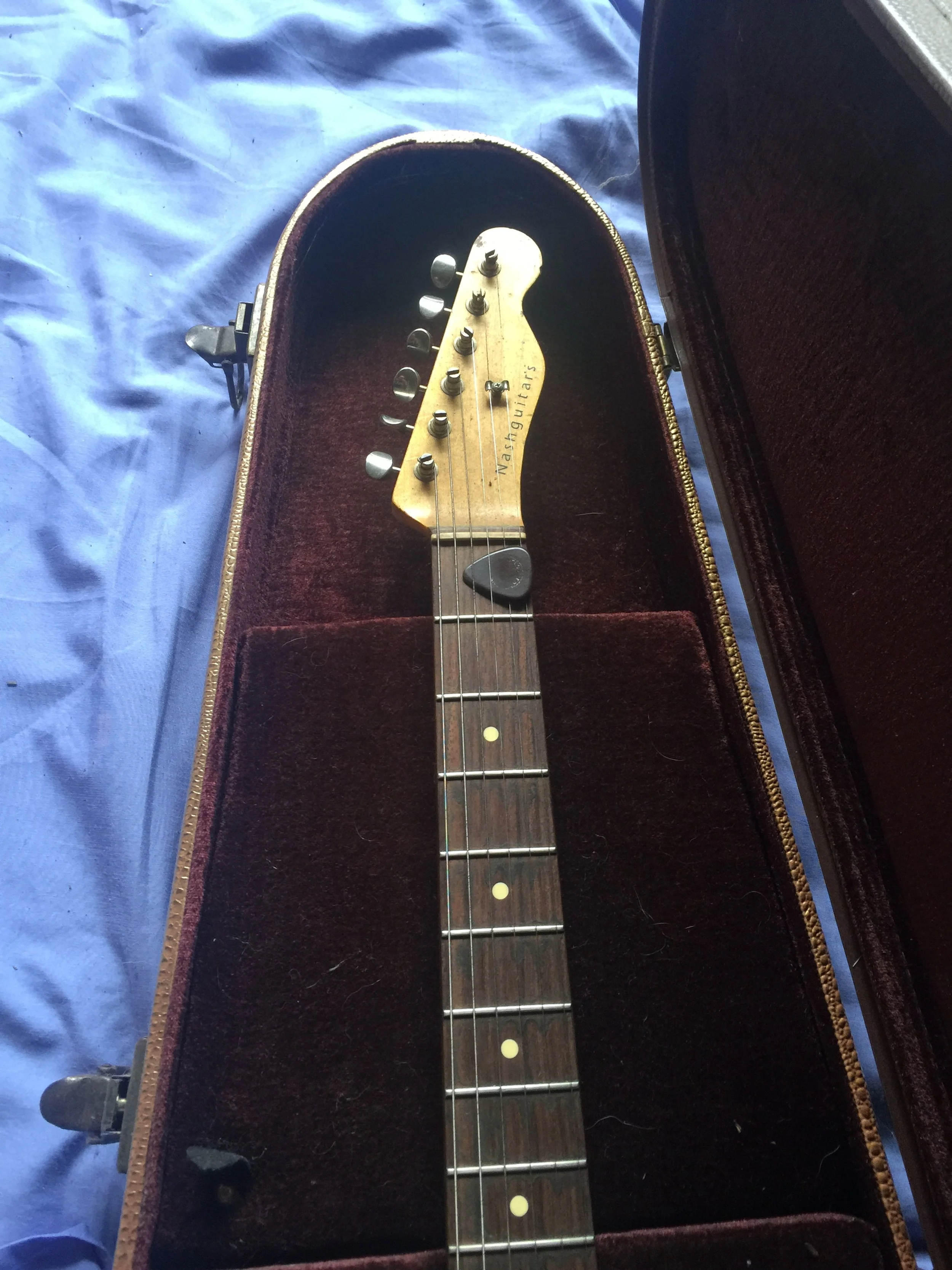 A vintage Wash Guitars electric guitar headstock inside a brown, velvet-lined guitar case on a blue fabric background.