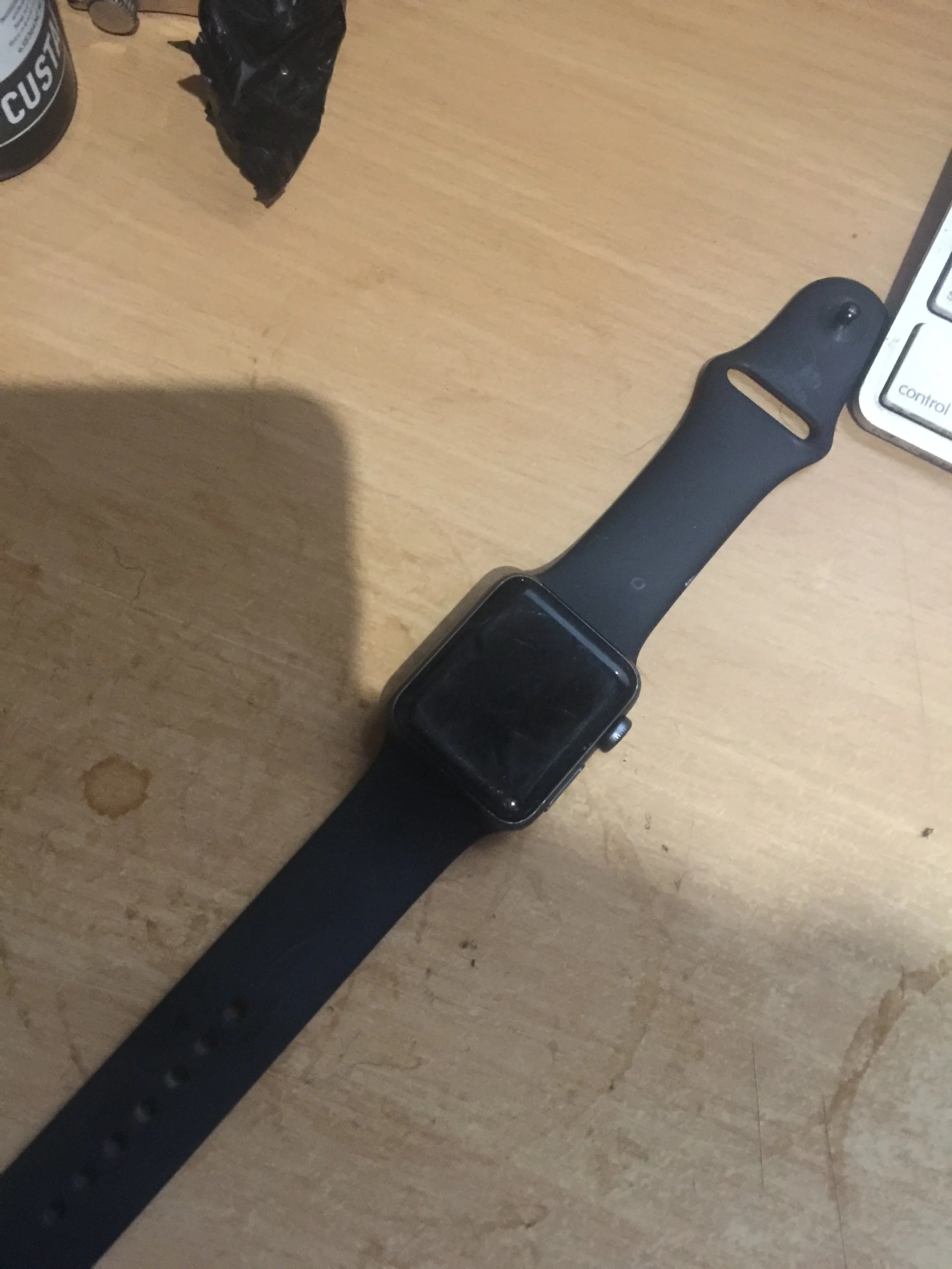 A black smartwatch with a rectangular face resting on a wooden surface.