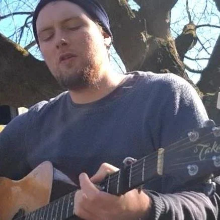 Young man playing an acoustic guitar outdoors.