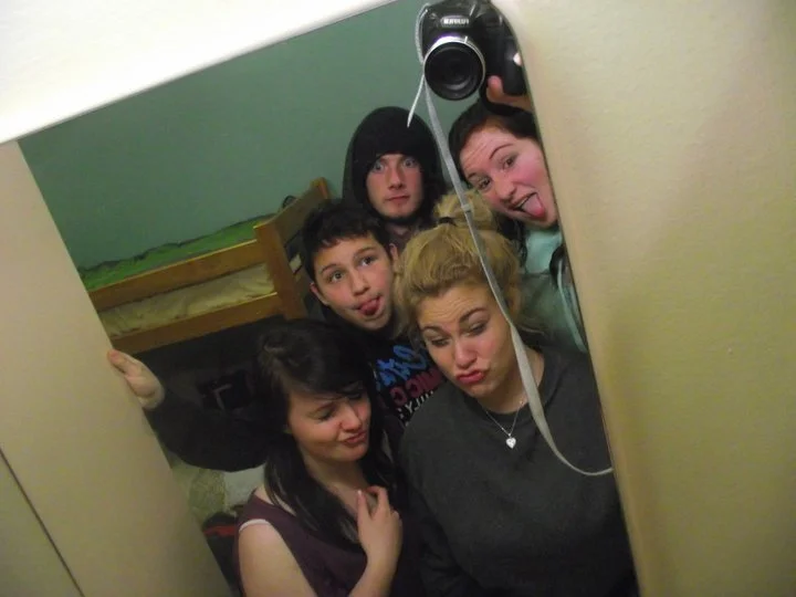Six young people taking a mirror selfie in a bedroom, making funny faces.