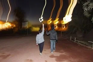 Two people walking away from the camera at night, with light trails above their heads.
