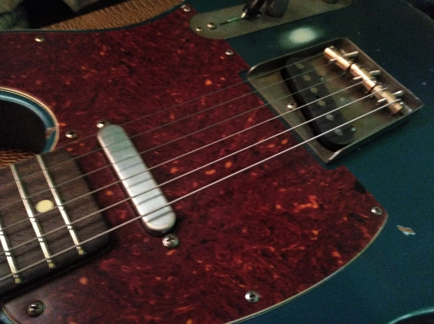 Close-up of a vintage electric guitar with a green body, a red tortoiseshell pickguard, and metal hardware including pickups and screws.