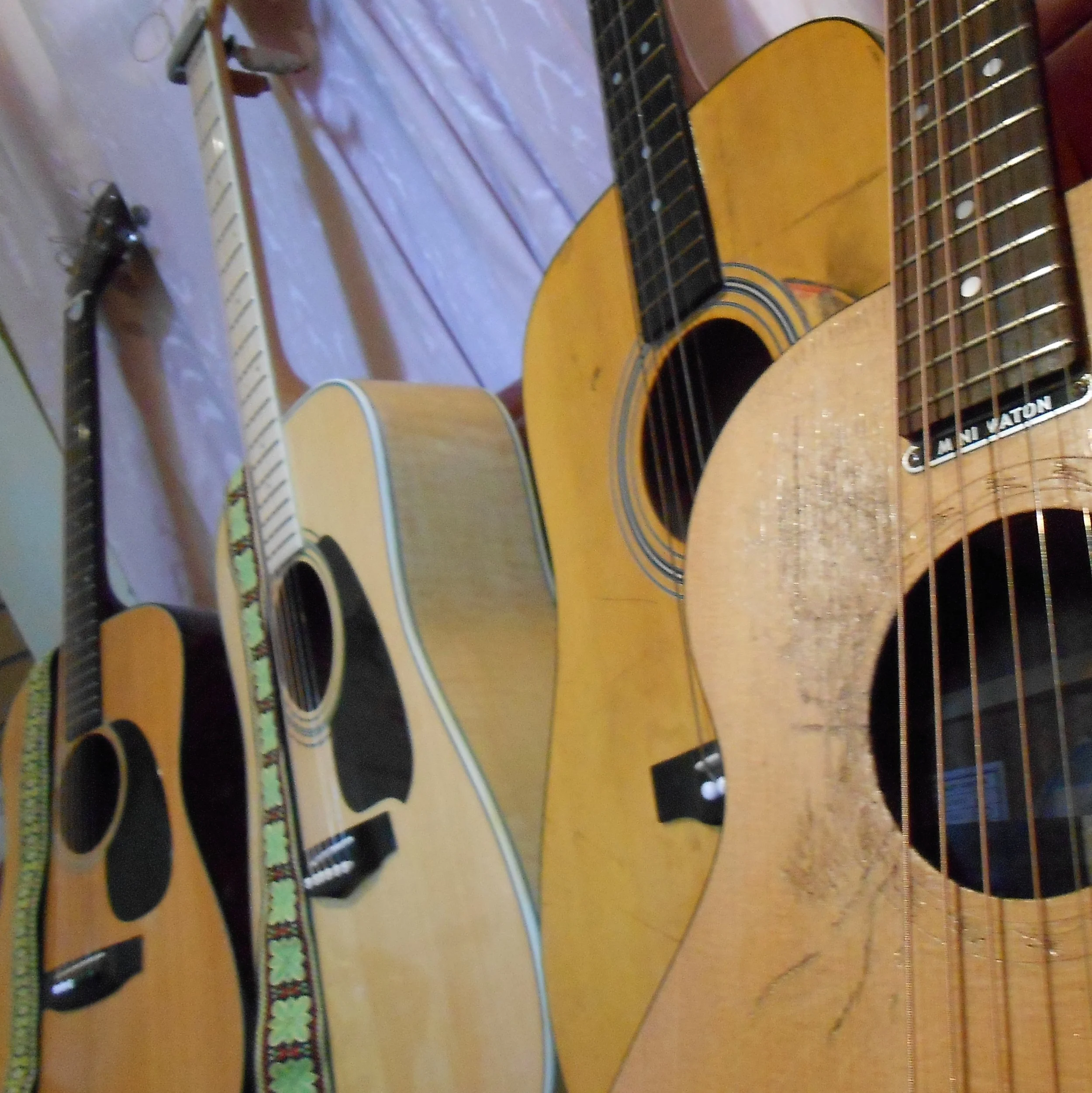 Multiple acoustic guitars placed on a purple bedspread.
