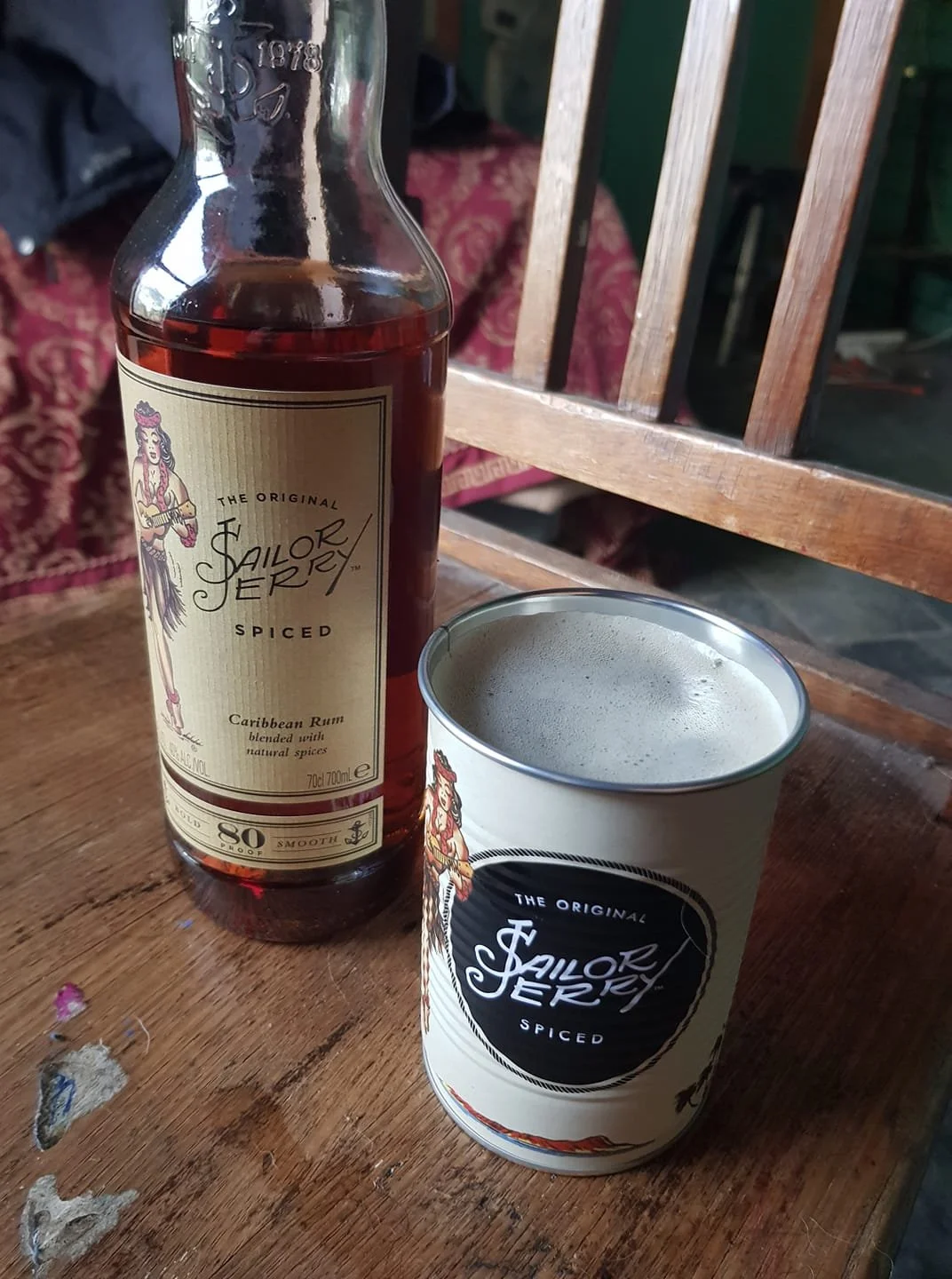 A bottle of Sailor Jerry spiced Caribbean rum and a metal can of Sailor Jerry spiced rum on a wooden table.