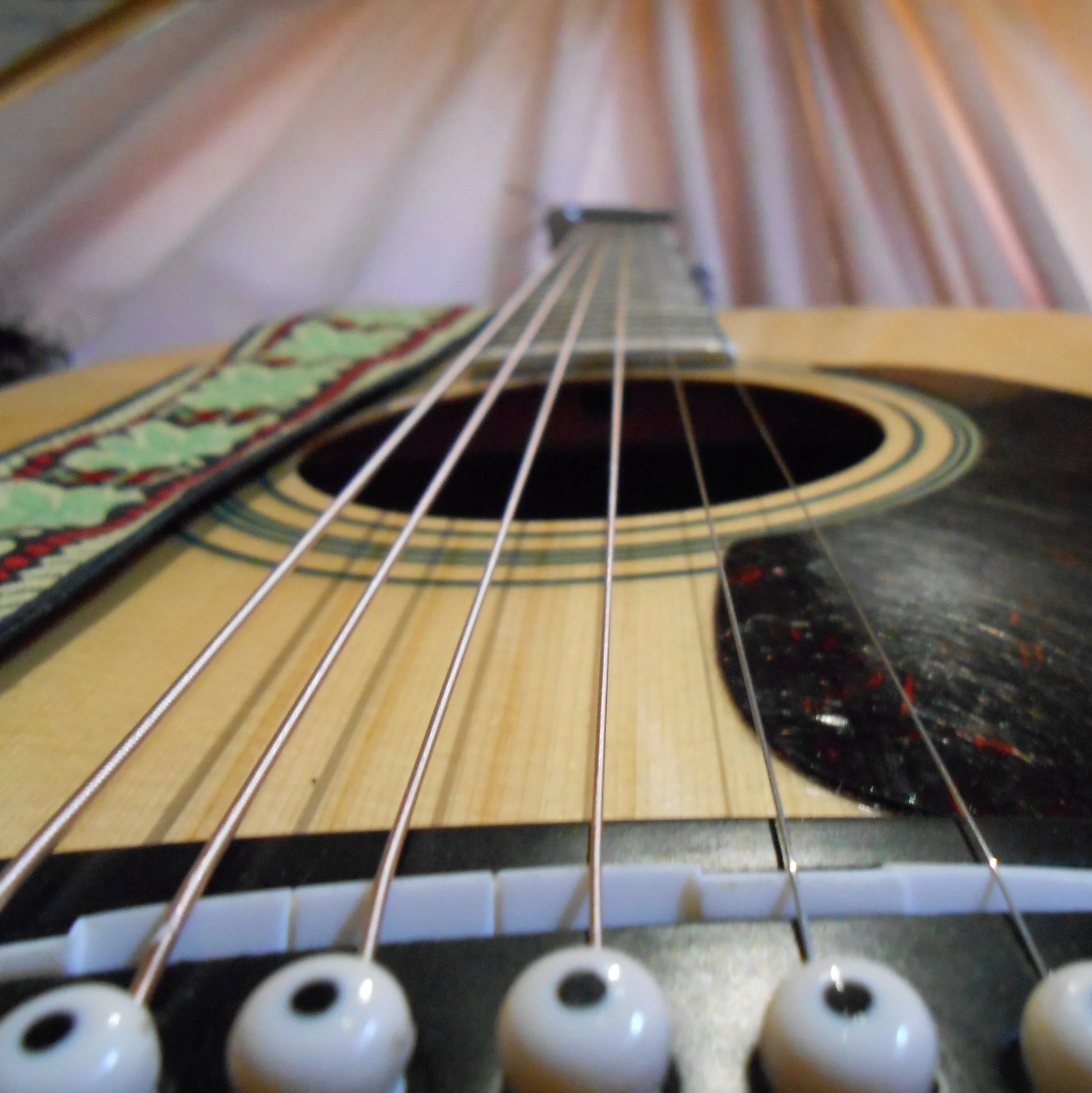 Close-up of an acoustic guitar taken from the bottom, showing the strings, sound hole, pickguard, and part of the neck.